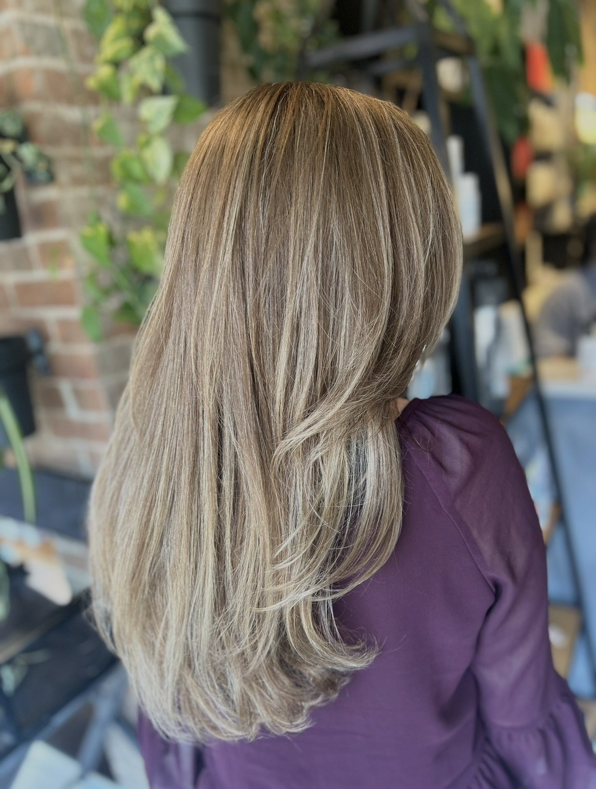 Back of a woman with long, wavy, blonde hair sitting in a salon or similar setting.
