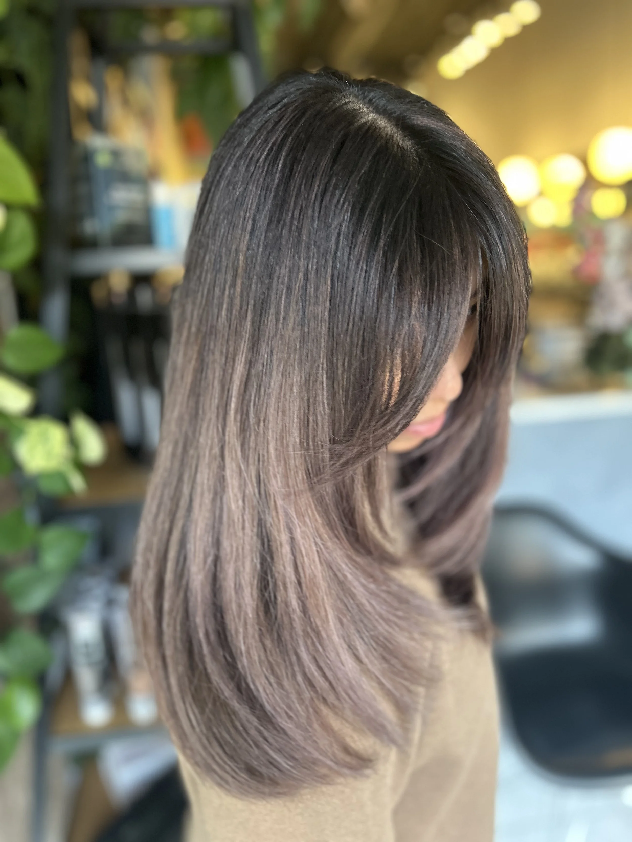 A woman with medium-length hair styled with layers and highlights, looking down in a salon or similar setting.