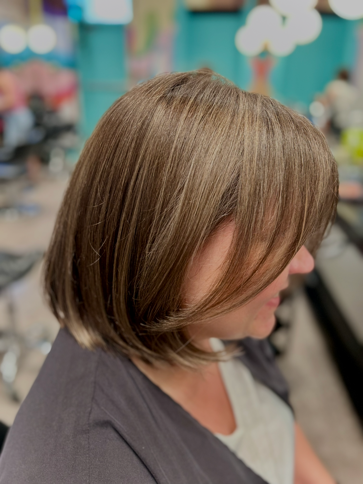 Side view of a woman with shoulder-length light brown hair sitting in a salon.