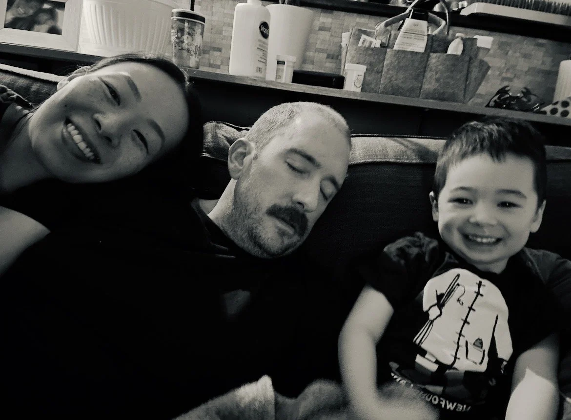 A woman, man, and young boy relaxing on a sofa, smiling and enjoying a happy moment together.