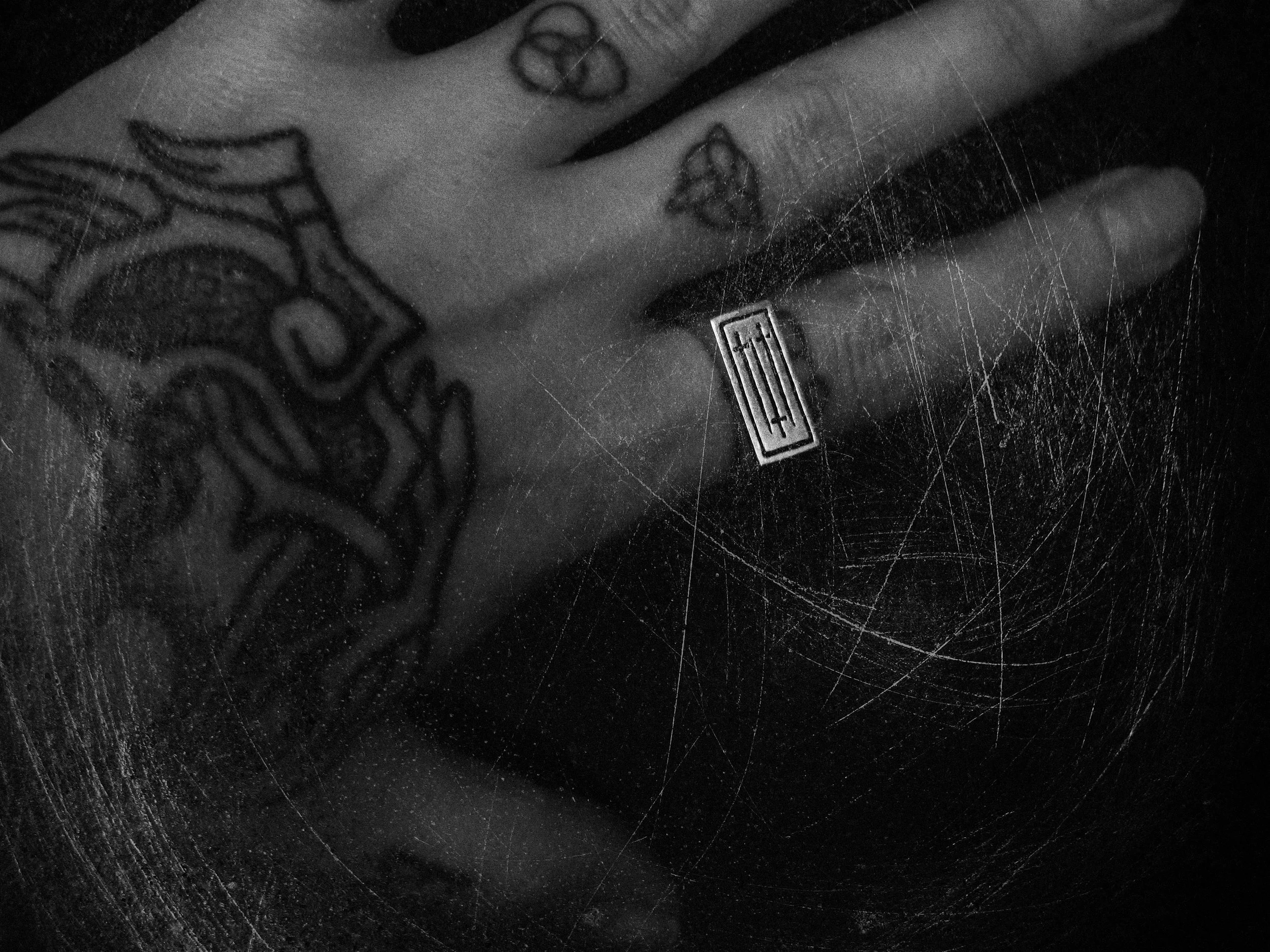 A black and white photo of a tattooed hand resting on a spiderweb.
