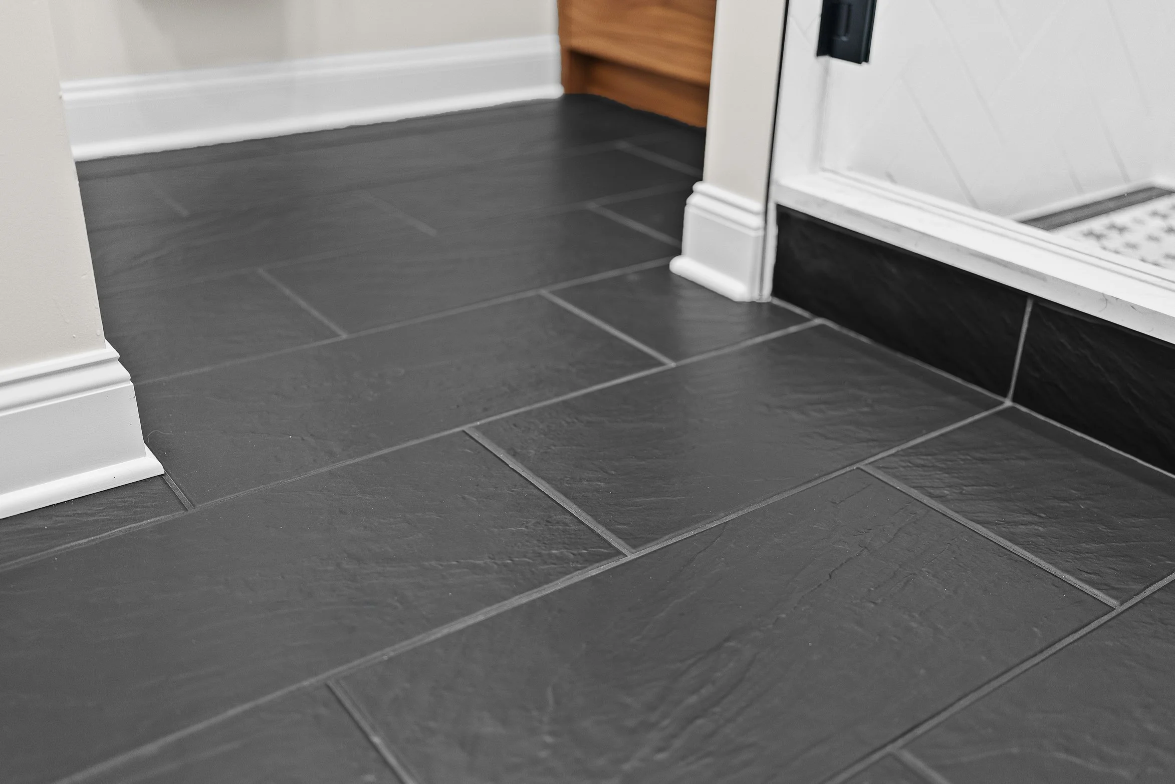 Close-up of black ceramic tile flooring with white and black baseboards near a doorway.
