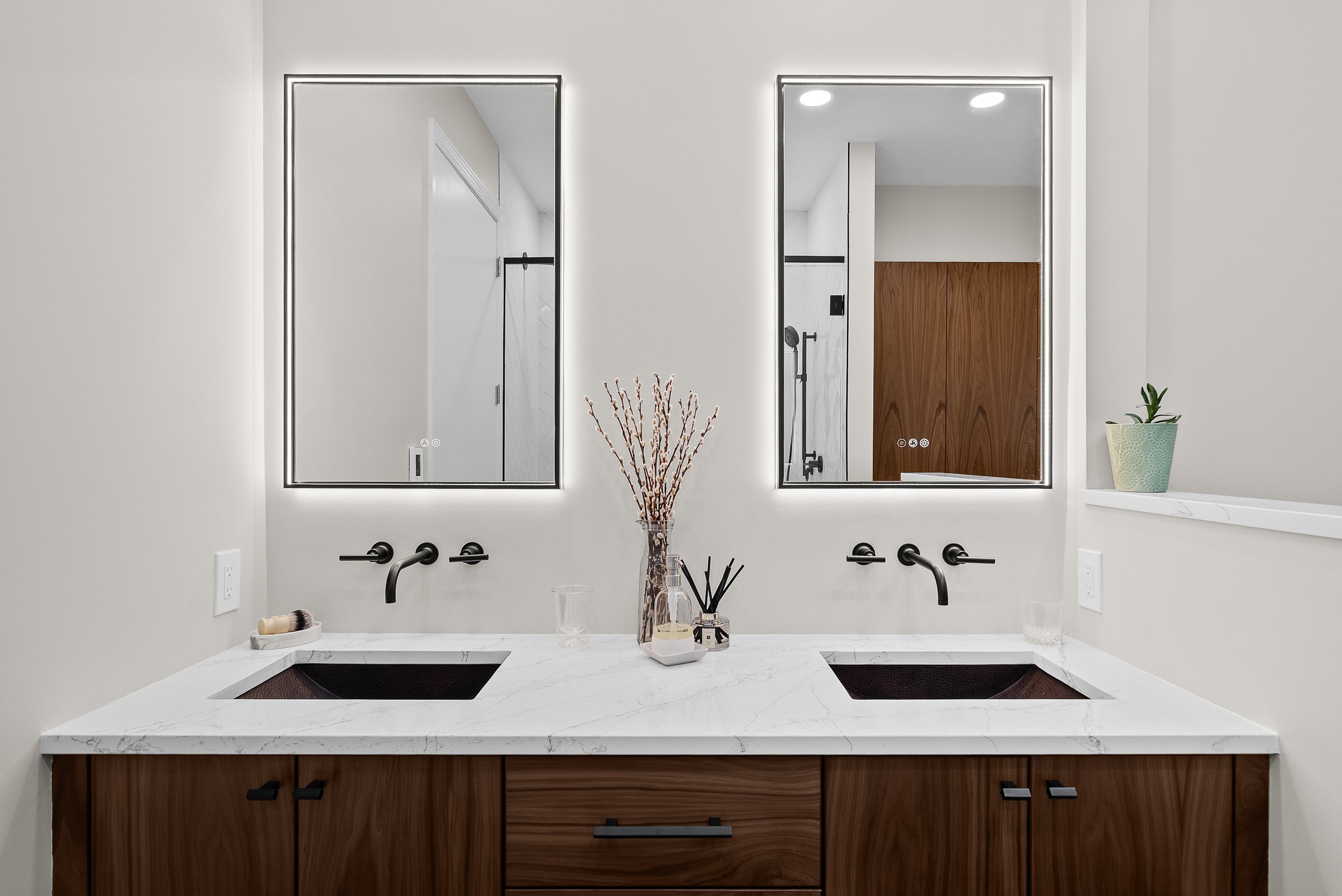 Modern bathroom double vanity with white marble countertop, black faucets, two large rectangular mirrors with LED lighting, and wooden cabinet drawers.