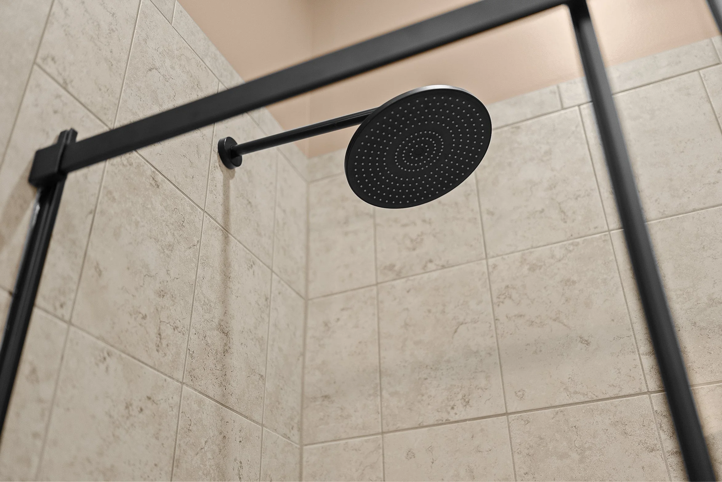 Close-up of a modern black showerhead mounted on a beige tiled shower wall.