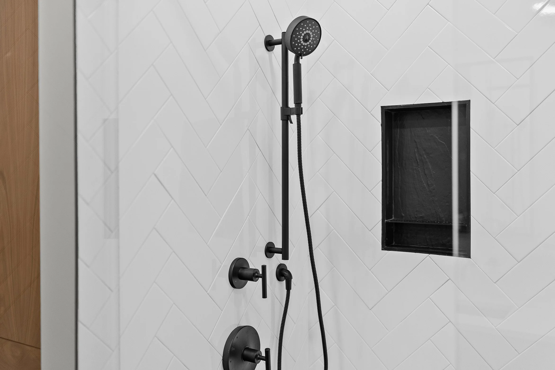 Close-up of a modern black showerhead and fixtures in a tiled bathroom shower with a built-in niche