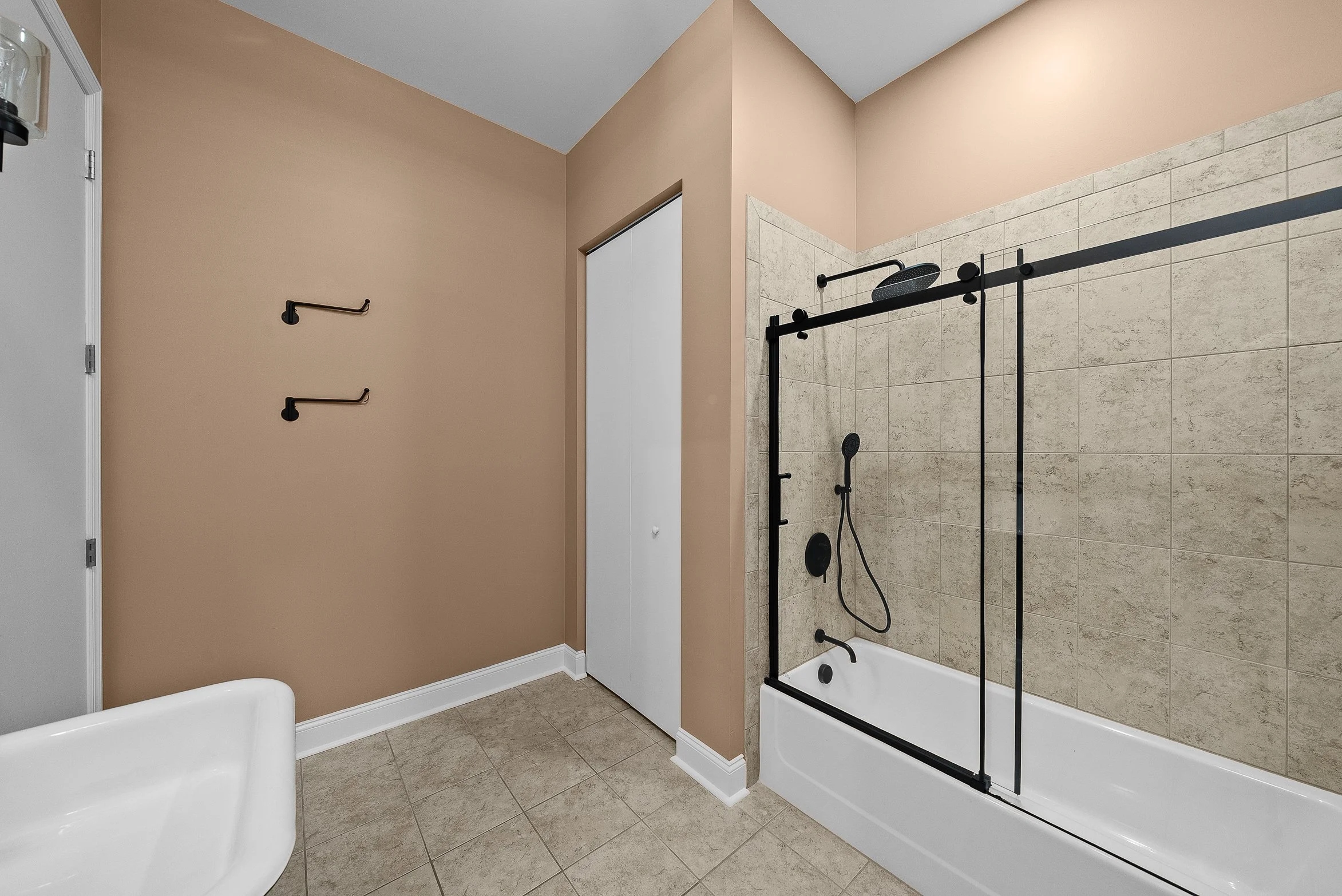 Bathroom with a beige wall, white sink, sliding door closet, and a walk-in shower with black fixtures and a glass door.