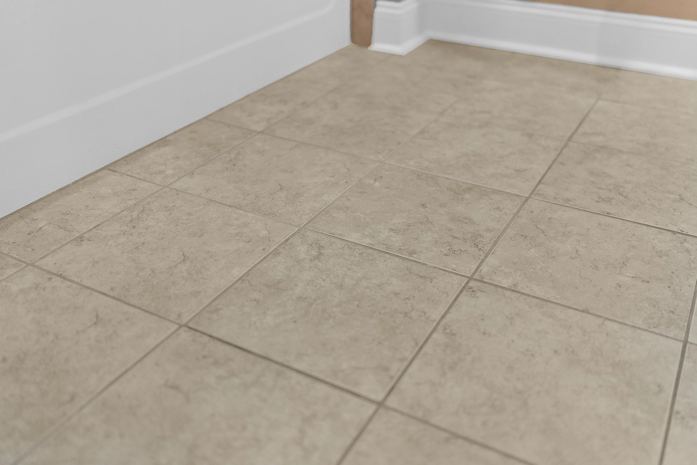 Close-up of beige ceramic floor tiles near a white wall and baseboard.