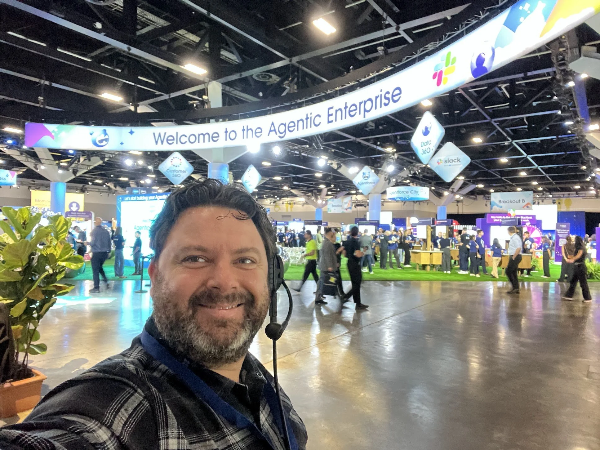 Man taking selfie at a conference with a large banner reading 'Welcome to the Agentic Enterprise' and various booths in the background.