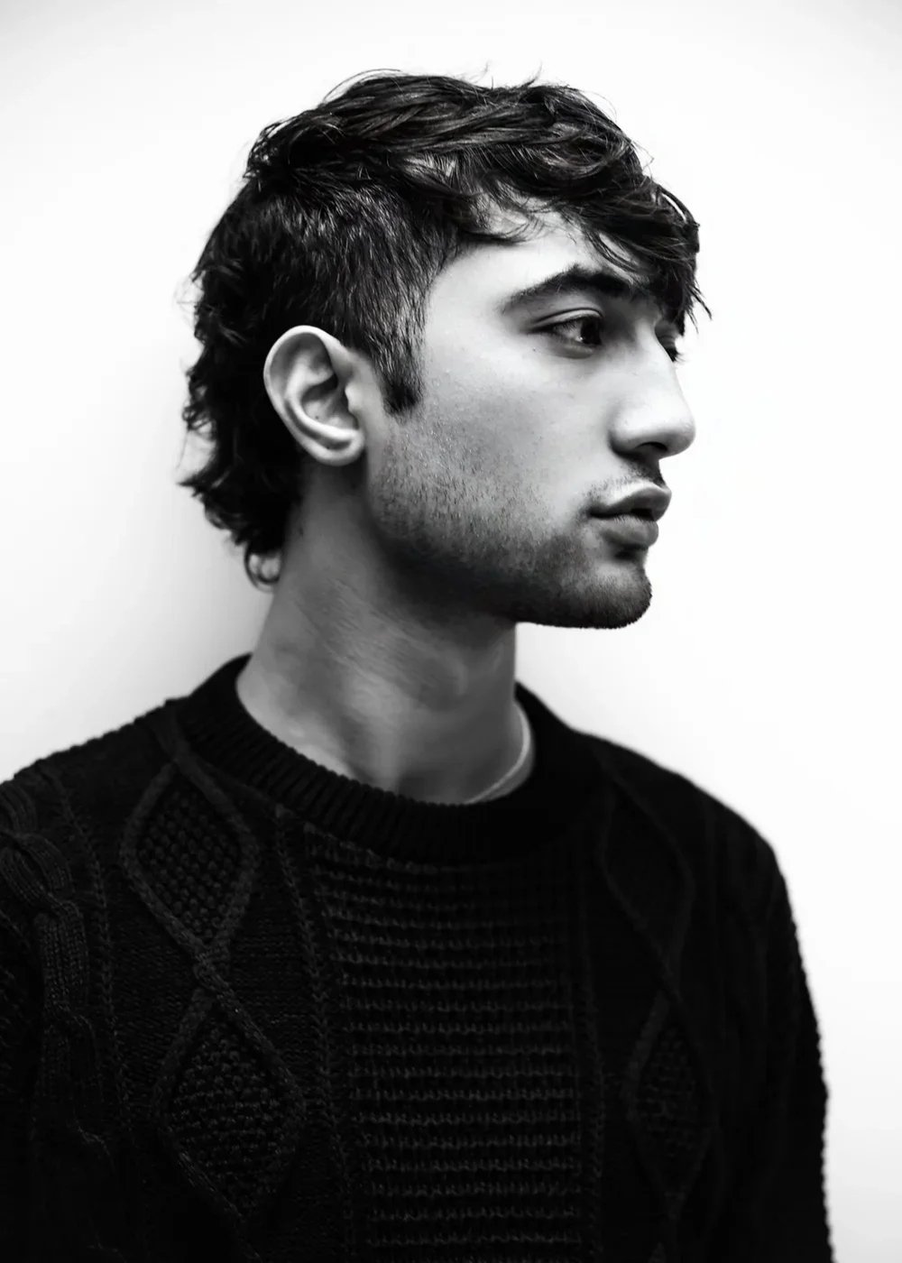 Black-and-white portrait of a young man in profile with a textured sweater, against a light background.