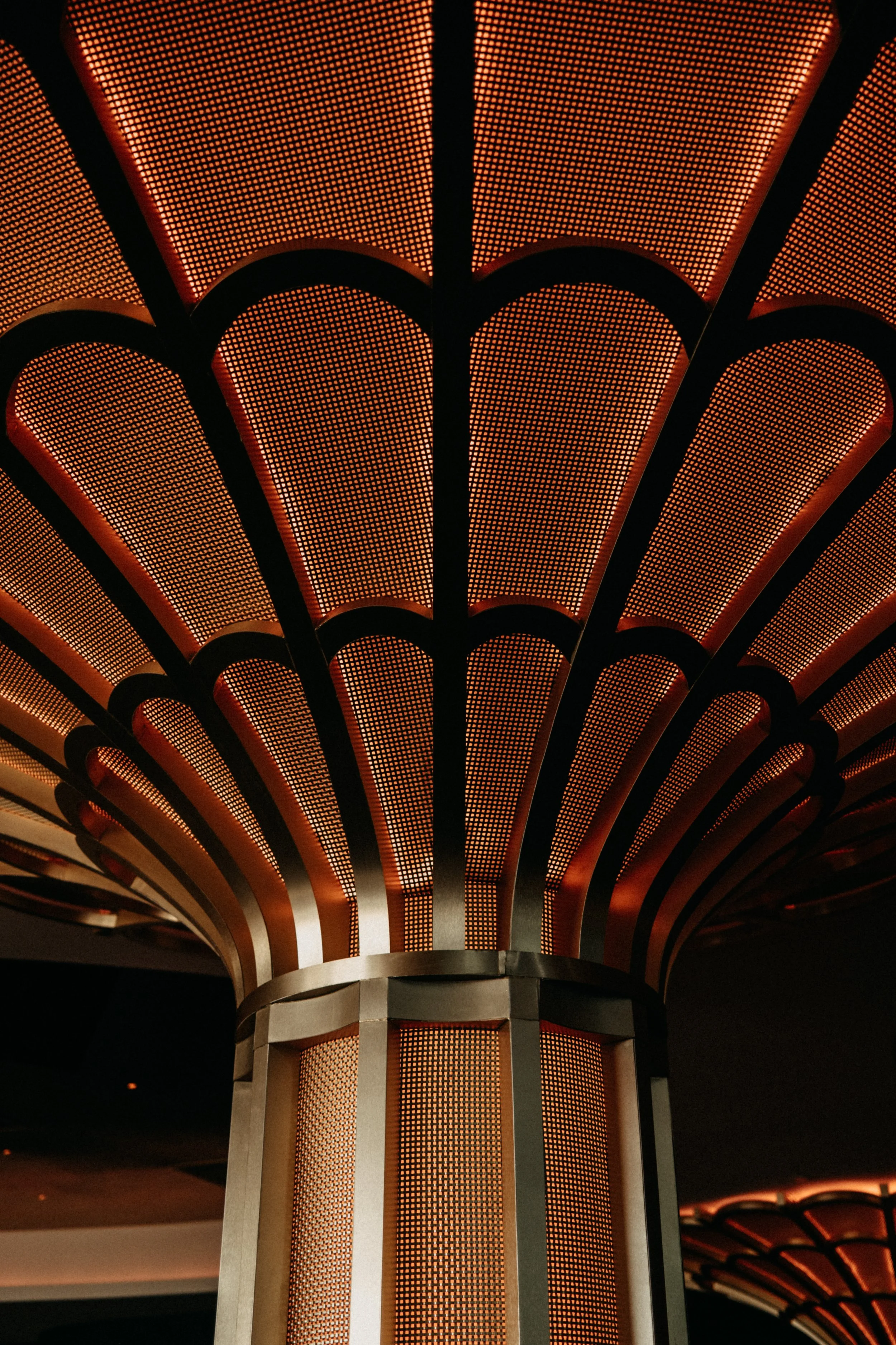 Close-up view of an ornate, illuminated ceiling structure with a pattern of small orange lights arranged in an arching design, supported by vertical metal elements.