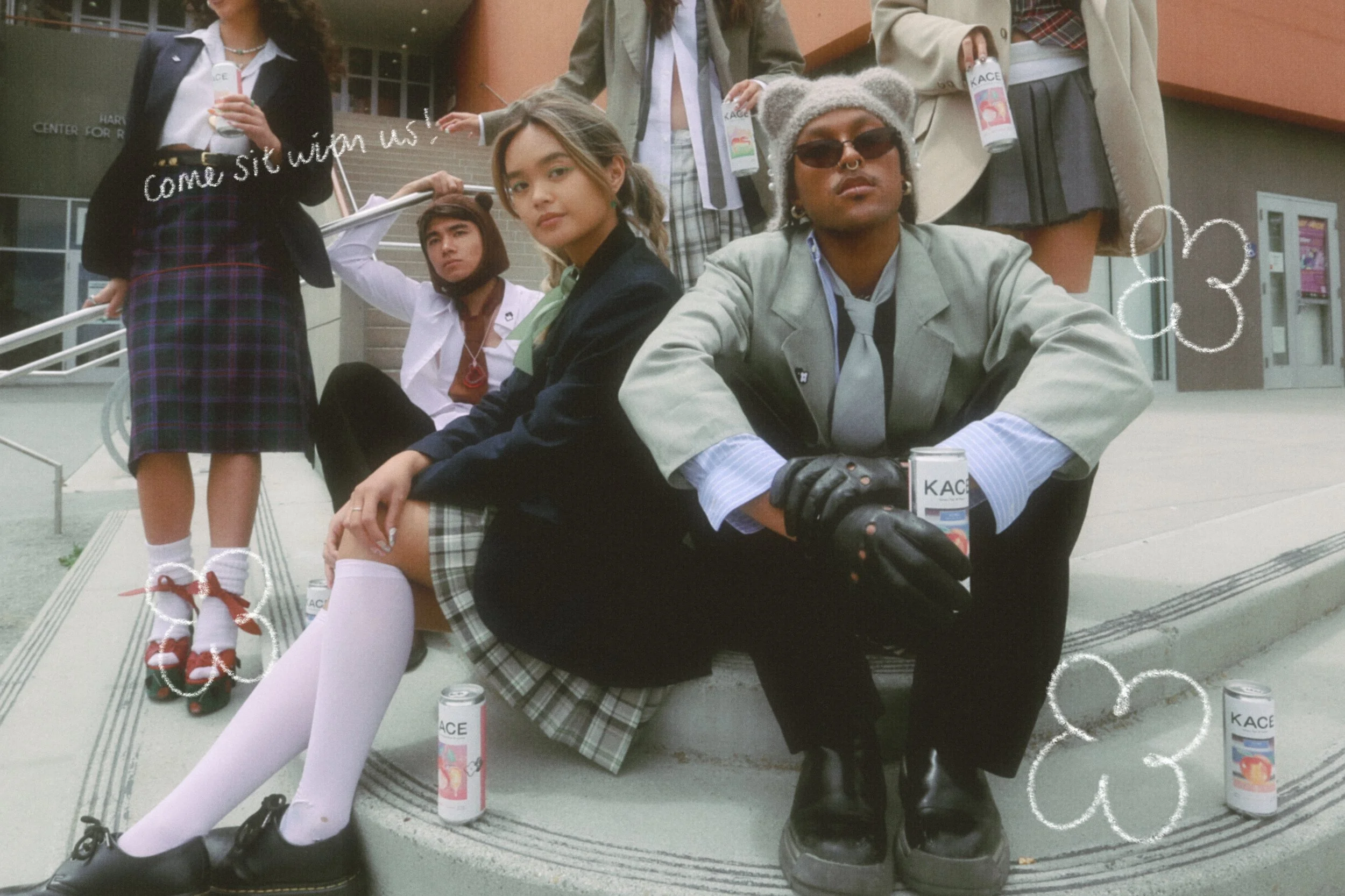 Group of young people in school uniforms sitting and standing outside a building. Some are holding cans of peach and apple juice, and a girl is wearing red shoes and white socks with bows. Handwritten-style doodles and text, 'come sit with us!', are 