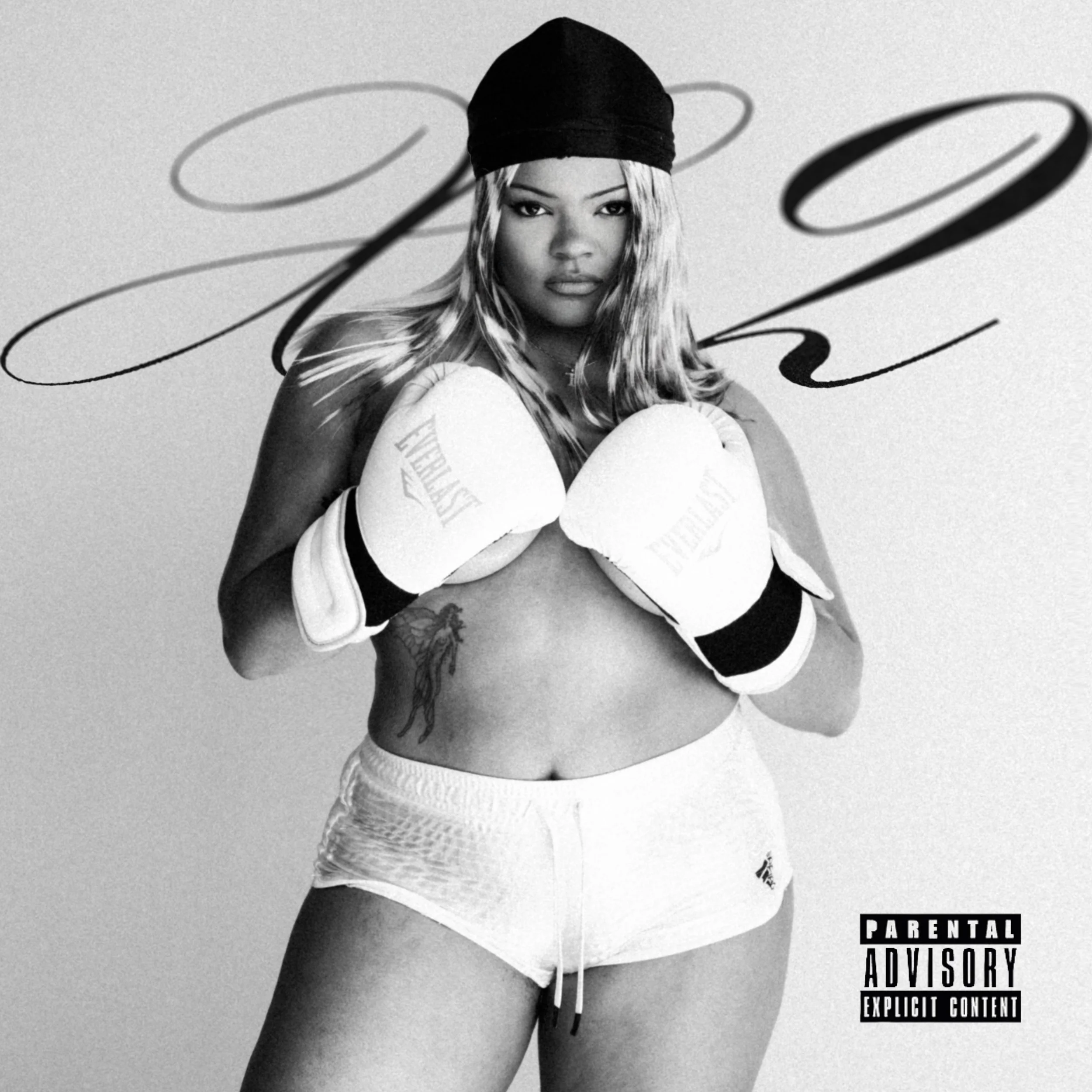 Black-and-white photo of a woman wearing boxing gloves, a headband, and shorts, standing with her fists raised. She has long hair, a tattoo on her side, and a serious expression. There is decorative script in the background and a parental advisory la