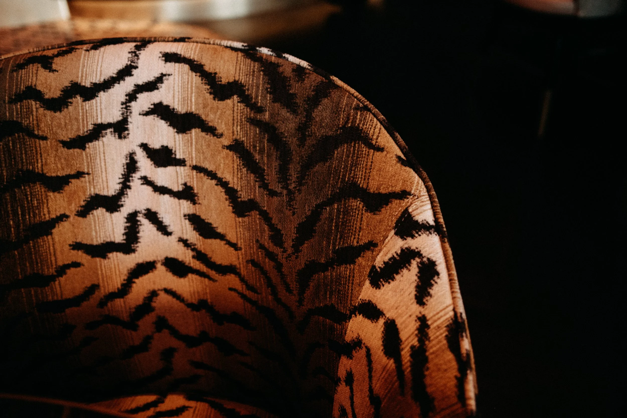 Close-up of a chair with orange and black patterned fabric, against a dark background.