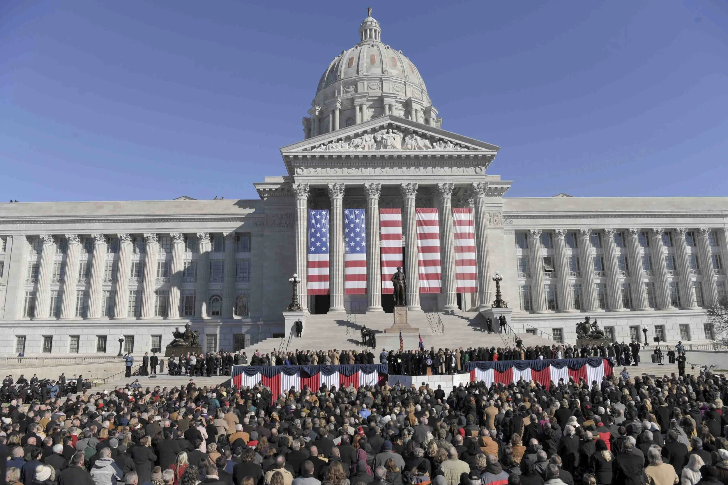 Crowd gathered outside the Capitol building, which is decorated with American flags and banners, during a patriotic event or ceremony.