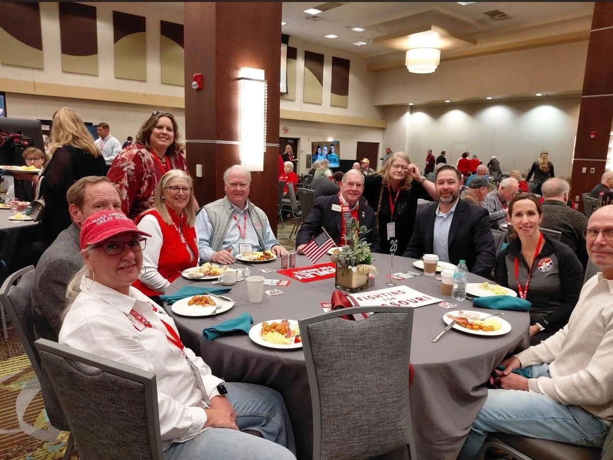 Group of people sitting around a table at a conference or event in a large banquet hall