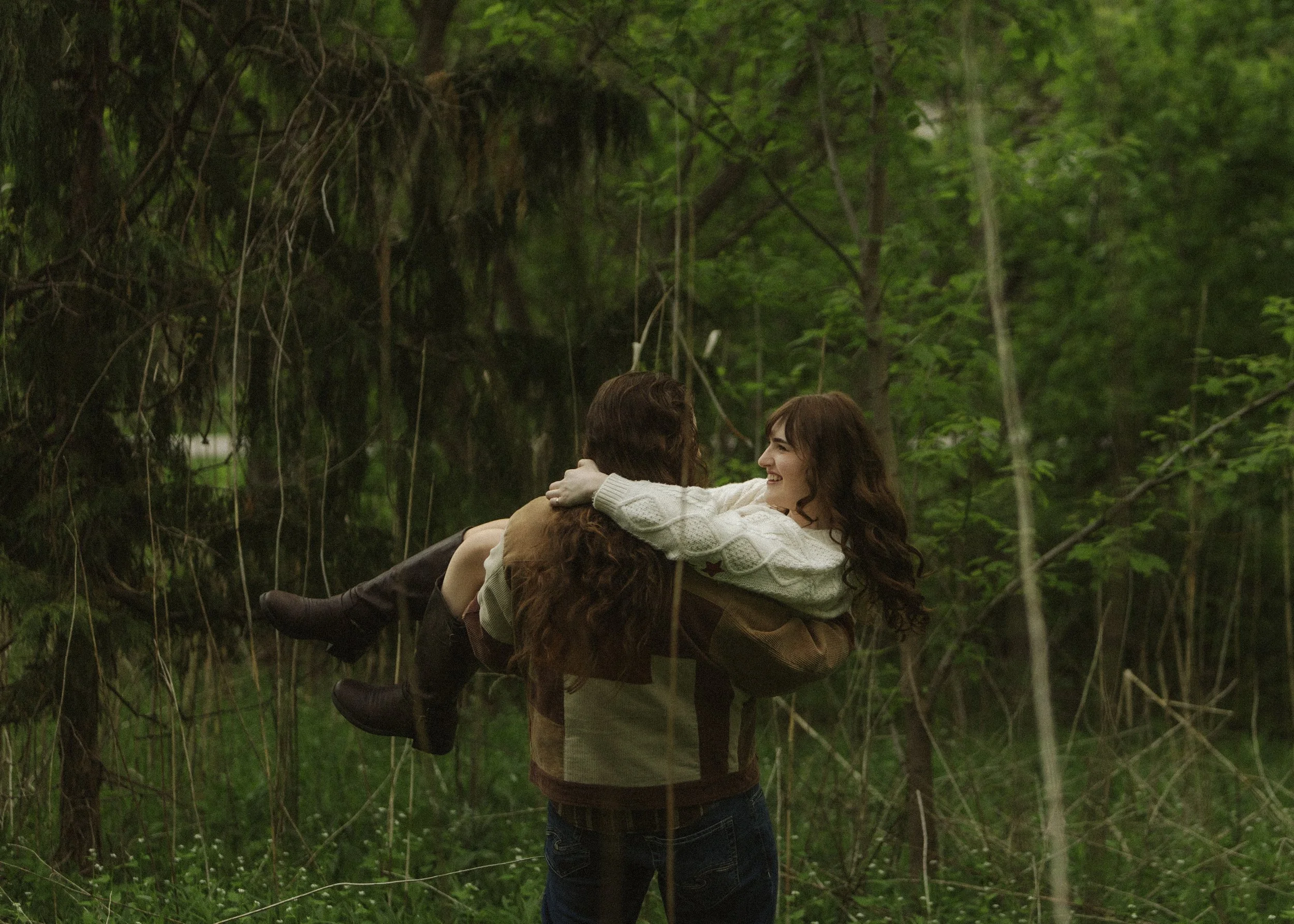 Two women embracing in a forested area with lush green trees and hanging vines.