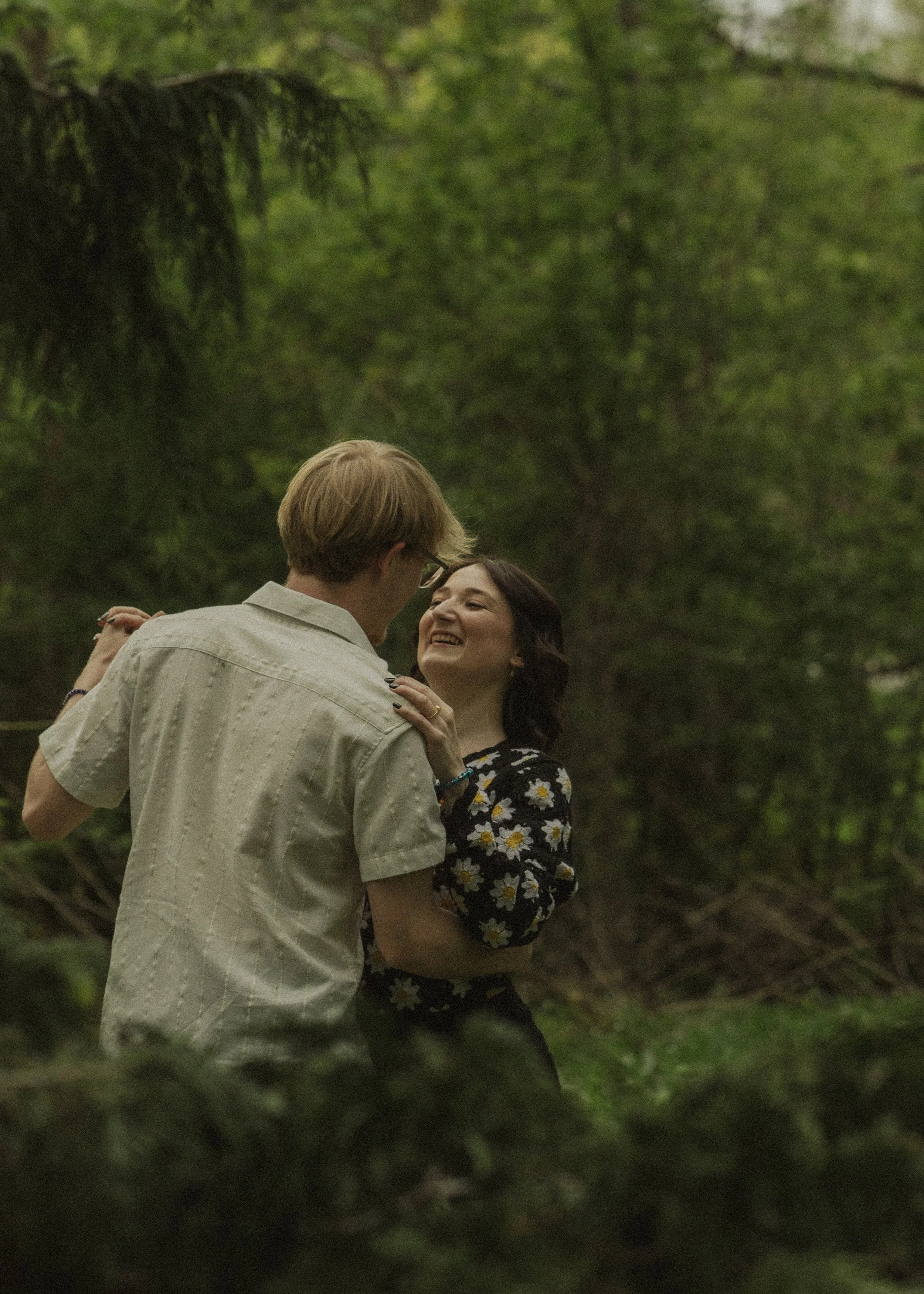 A couple dancing outdoors in a lush green forest, smiling at each other.