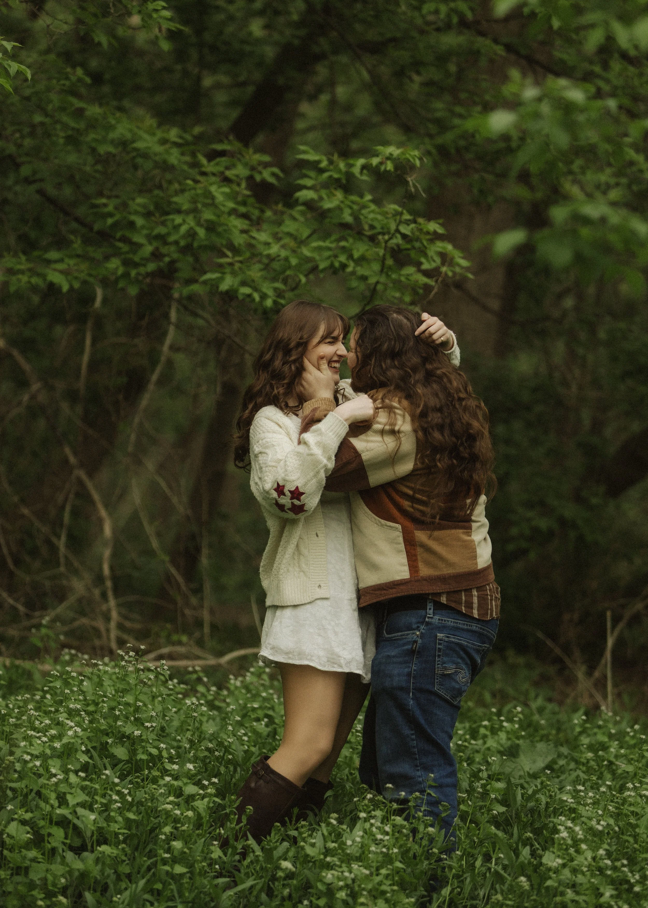 Two women in a forest, smiling, holding each other.