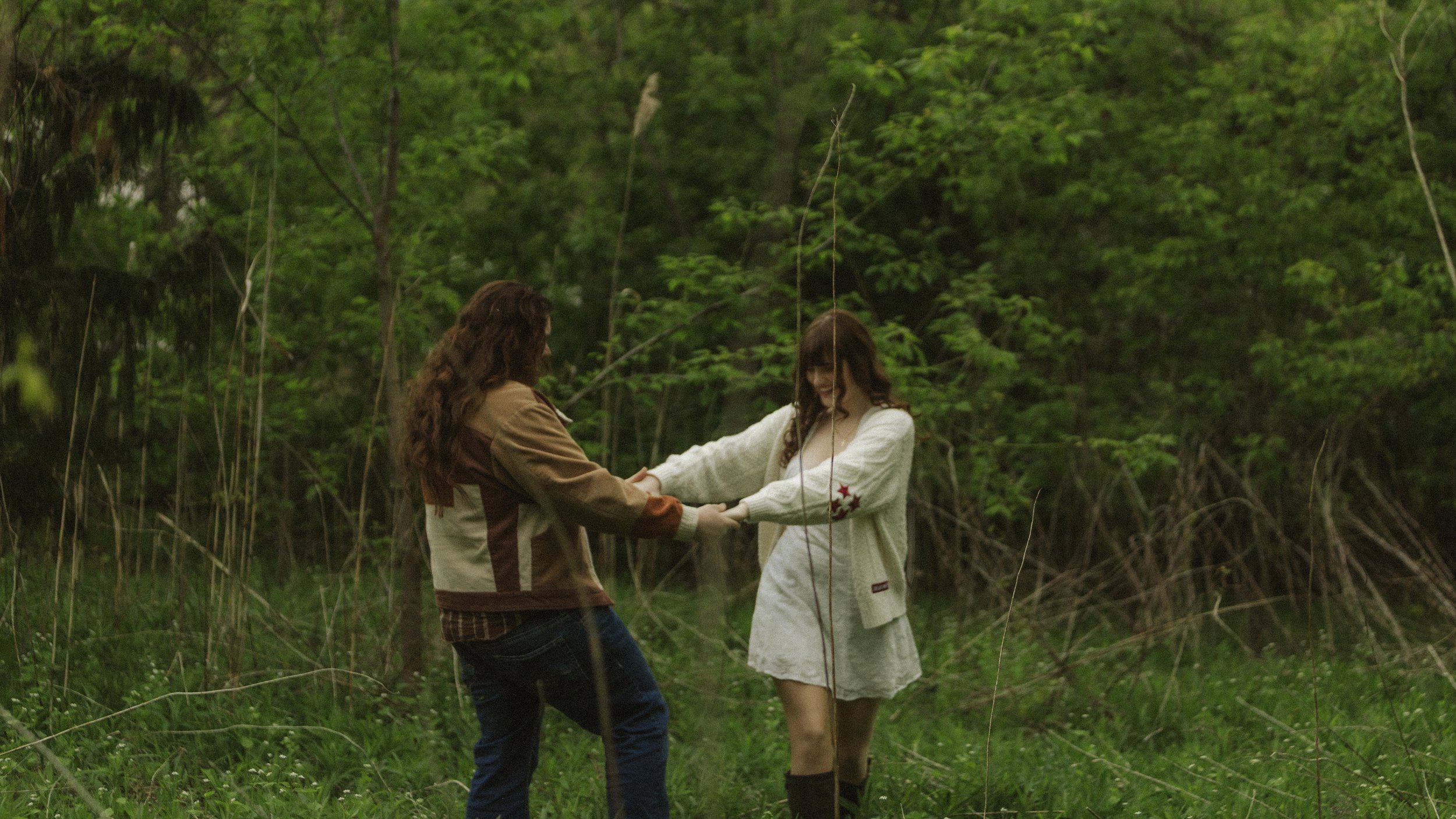 Two women holding hands and smiling in a lush green forest.