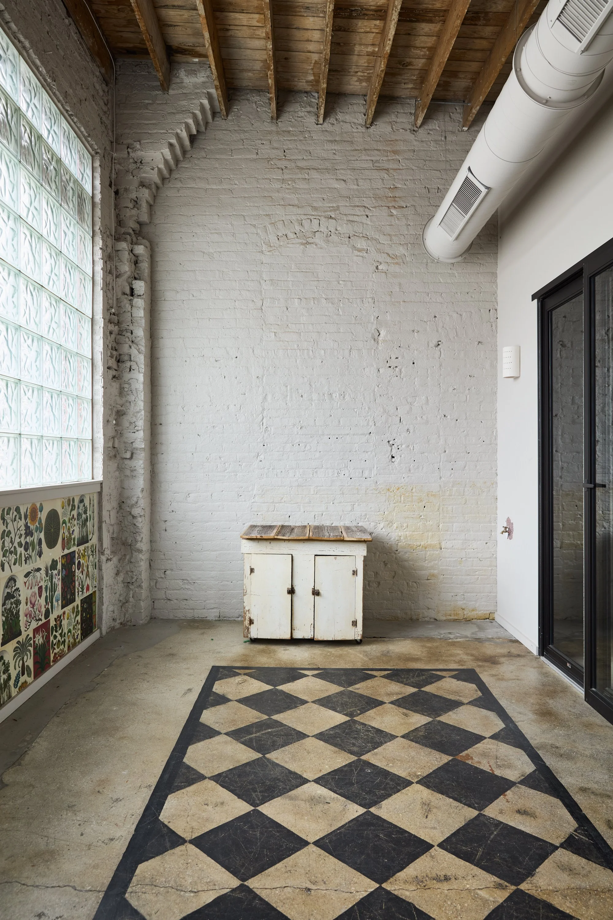 Beautiful neutral textures like the white brick wall, concrete floor, and wooden ceiling, along with plenty of natural light from the glass block window make this room a dream for portraits, small tabletop or content creation at Green Relish Studio.
