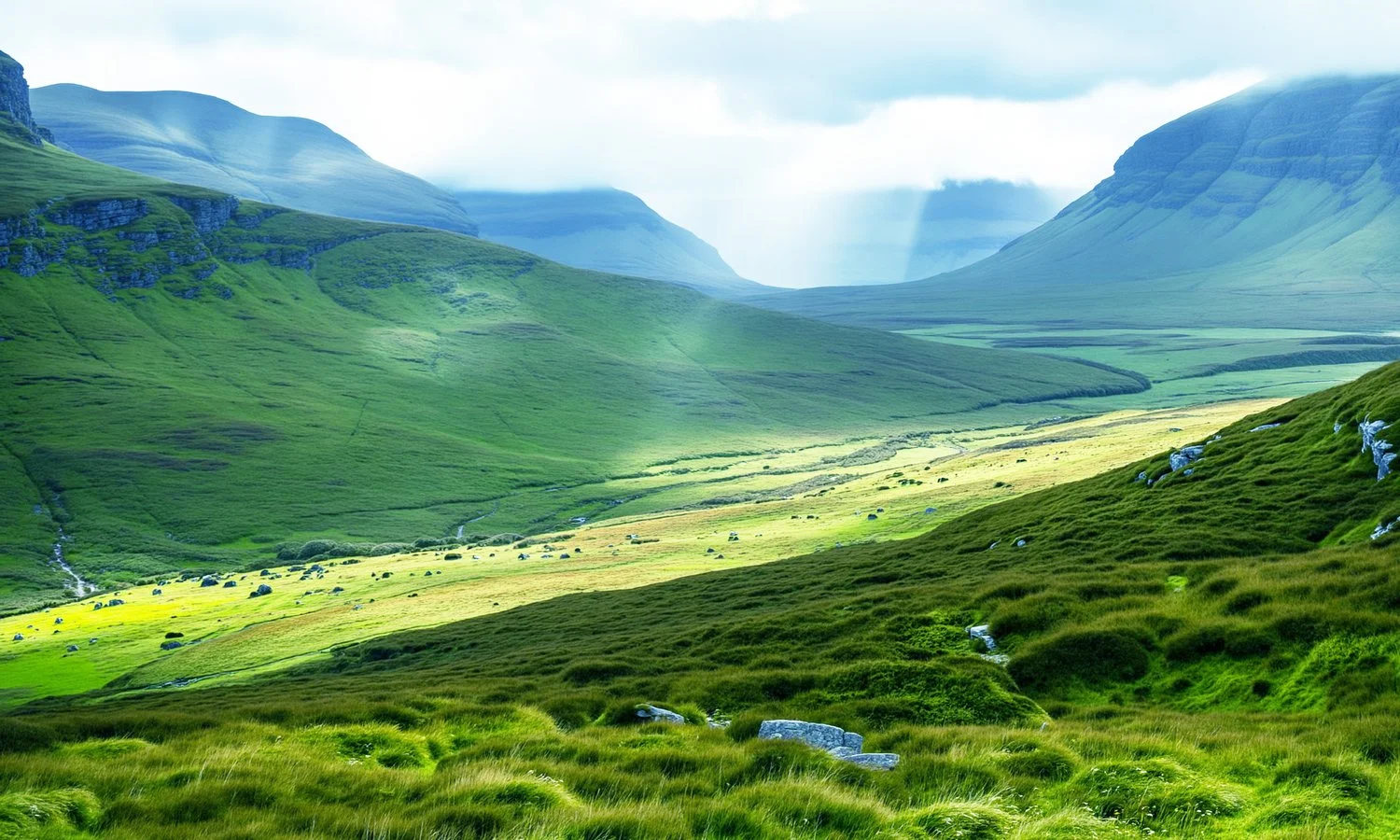Lush green rolling hills and mountains with a cloudy sky and some sunlight rays.