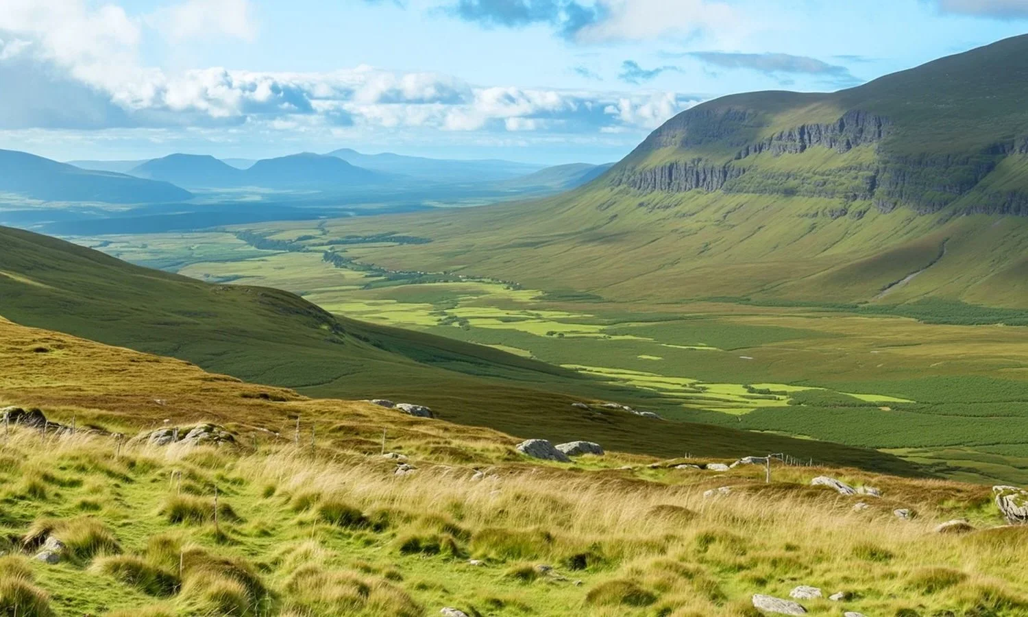 Scenic view of a lush green valley surrounded by rolling hills and mountains under a partly cloudy sky.