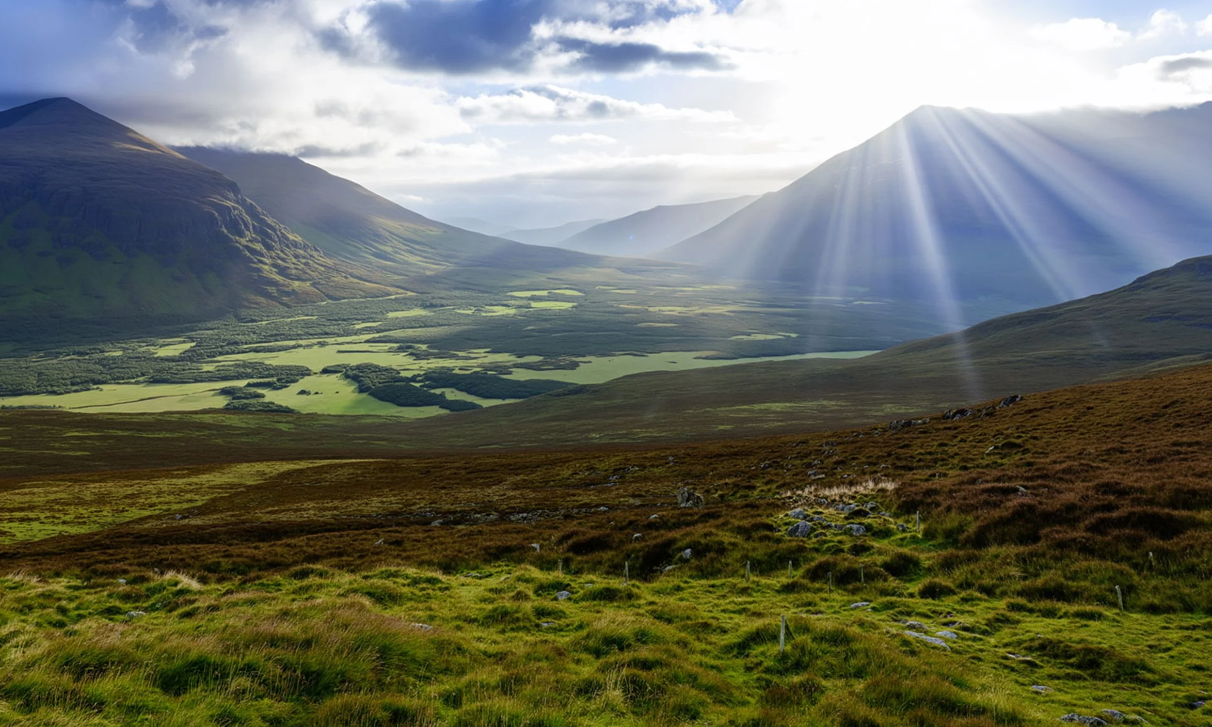 Sun rays shining over a lush green valley surrounded by mountains in the distance.