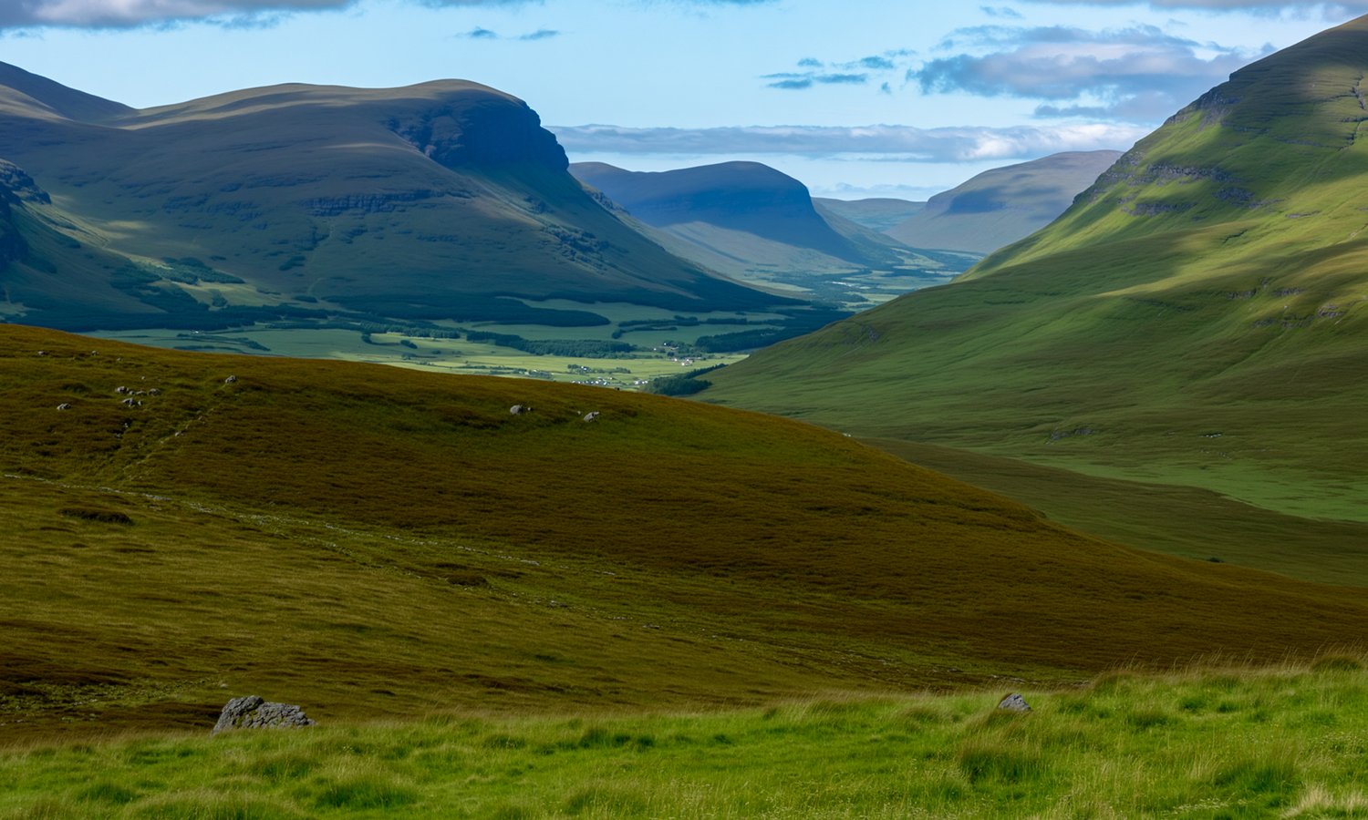 A scenic view of a green valley surrounded by rolling hills and mountains under a partly cloudy sky.
