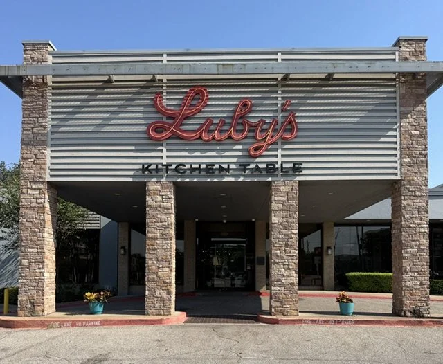 Front of Luby's restaurant with stone pillars and a sign that reads "Luby's" in red script, and "Kitchen Table" in black letters below.