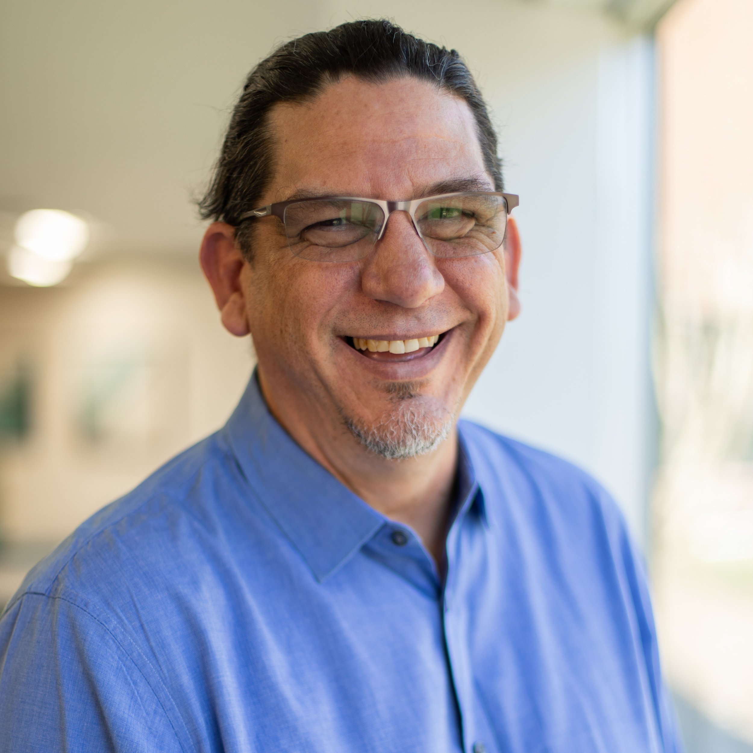 Close-up of smiling man wearing glasses and a blue shirt.