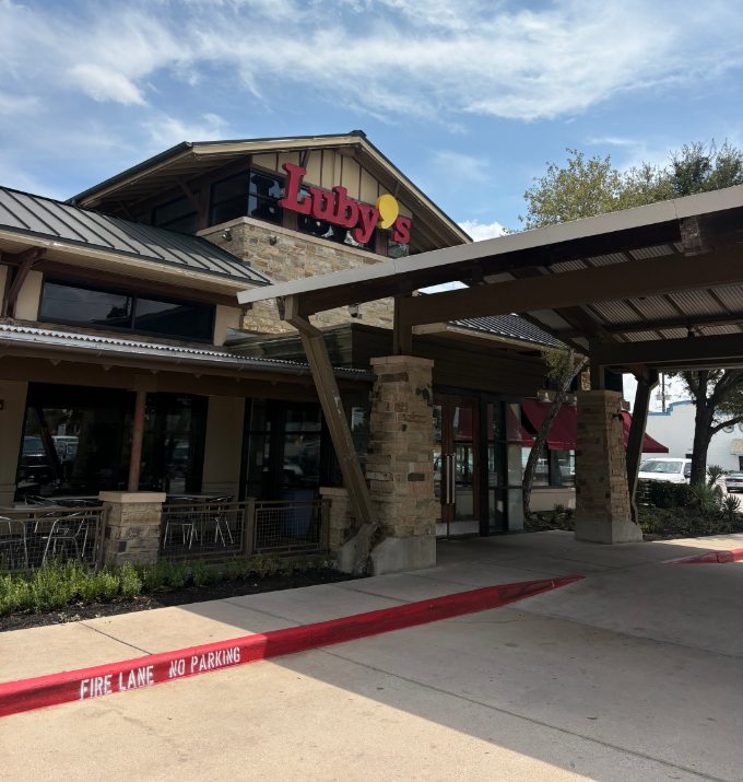 Luby's restaurant with stone and wood exterior, red signage, outdoor seating area, and a fire lane with no parking marked in red.
