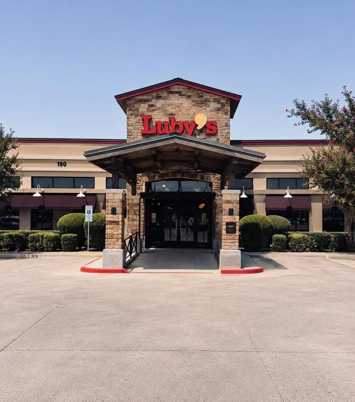 Front entrance of Luby's restaurant with a stone facade, covered porch, and greenery.