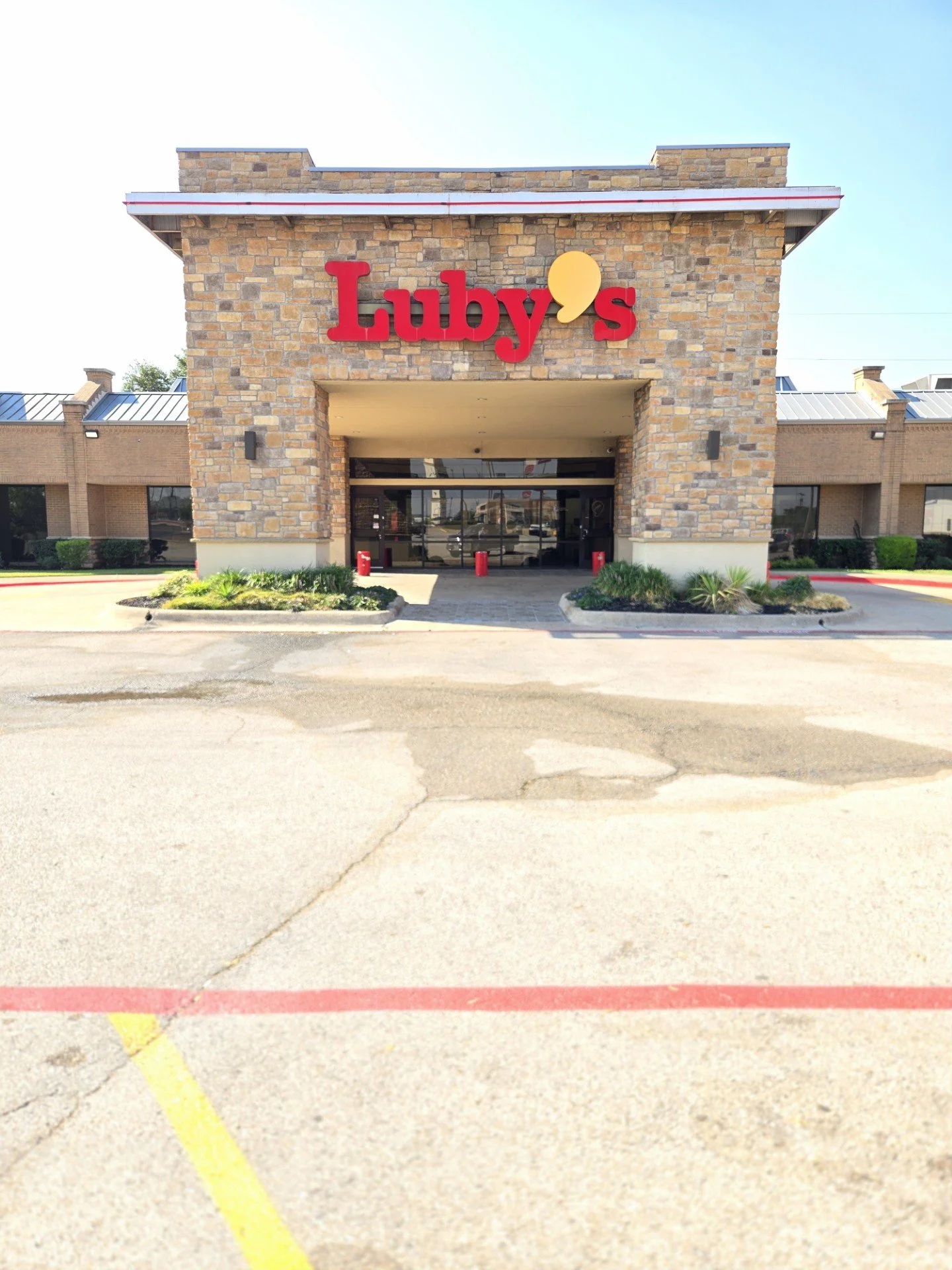 Exterior view of a brick building with a large red sign that says "Luby's" and a yellow punctuation mark, with a parking lot in the foreground.