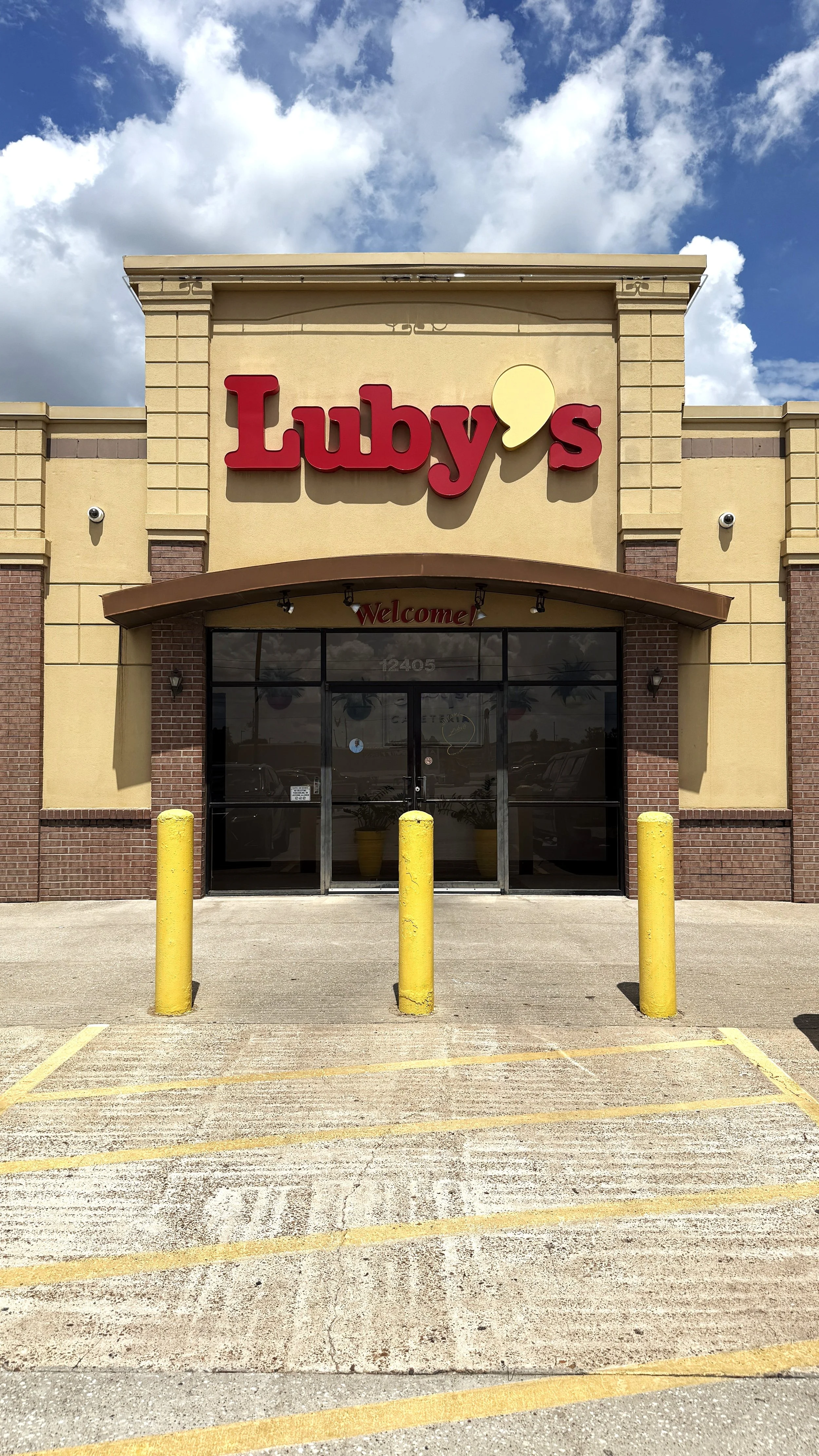 Front of a restaurant named 'Luby's' with a sign above the entrance, yellow pillars in front, and an empty parking lot.