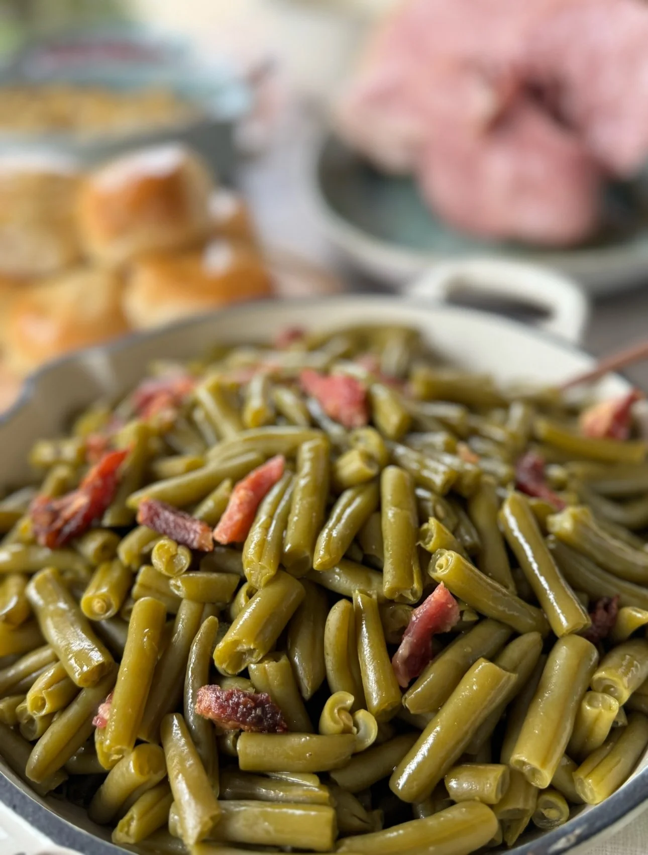 Close-up of a bowl filled with cooked green beans and sliced bacon.
