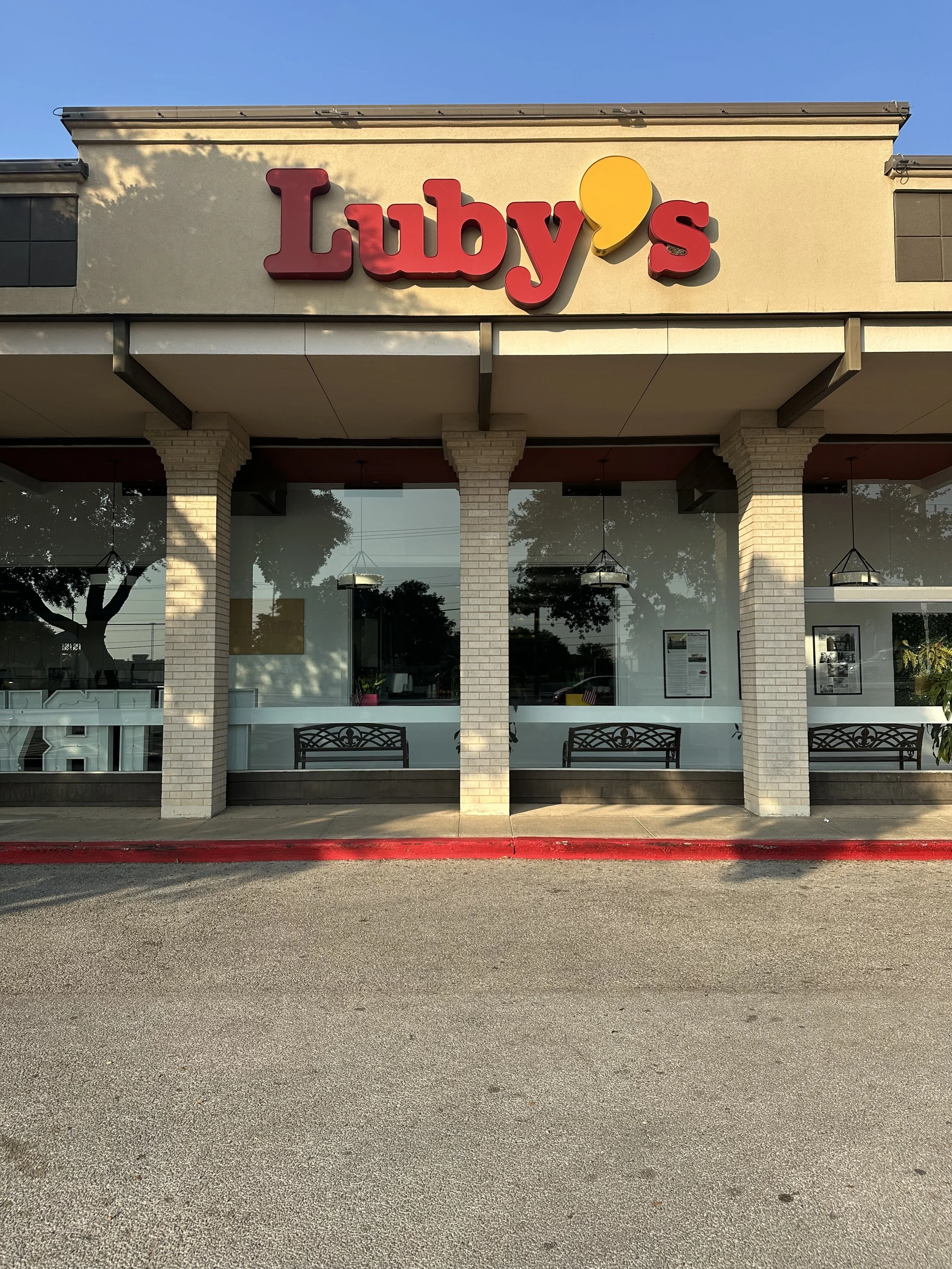 Exterior of a Lily's restaurant with a large sign, large glass windows, and brick pillars, situated along a paved street with a red-painted curb and parked cars reflecting in the windows.
