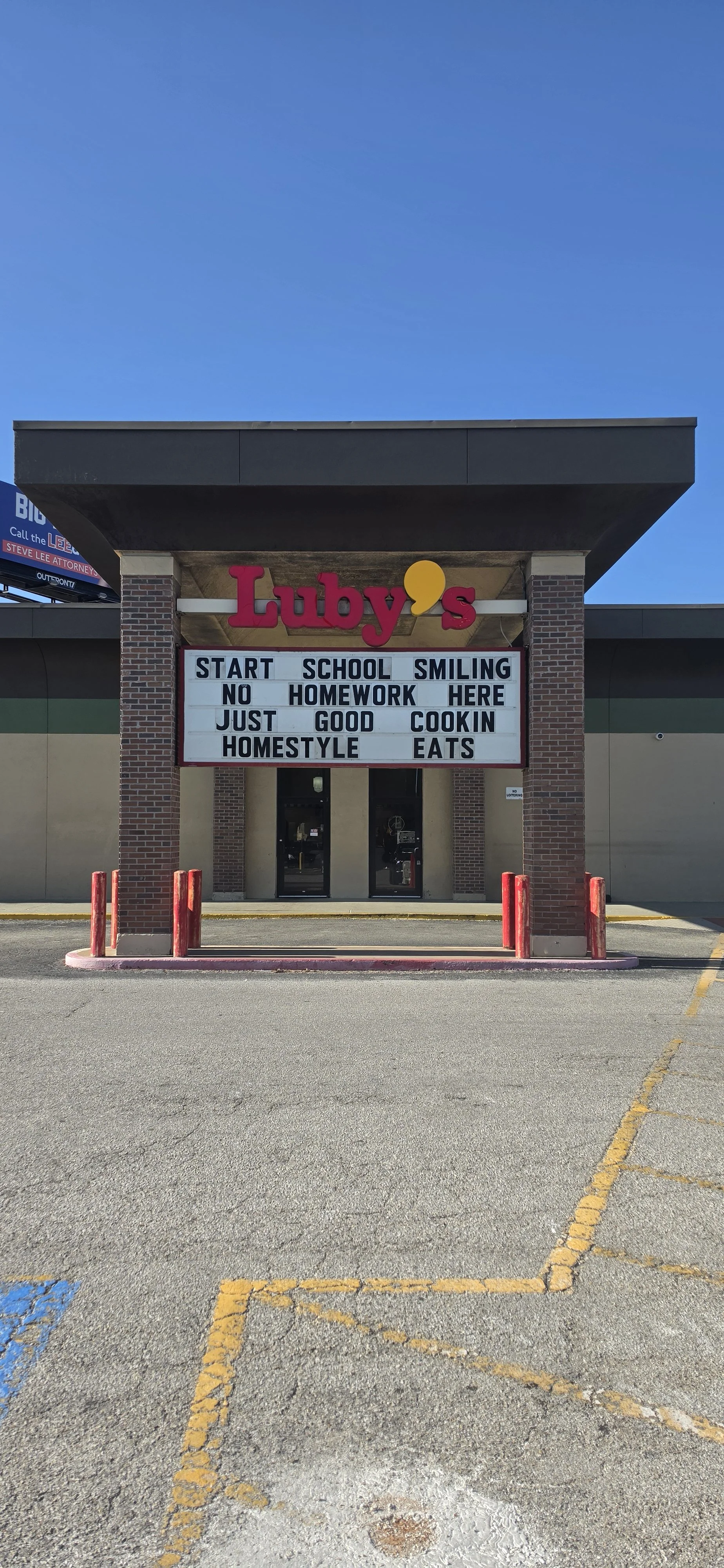The exterior of a restaurant called Luby's with a sign that reads, 'Start school smiling no homework here just good cookin homestyle eats,' under a clear blue sky.