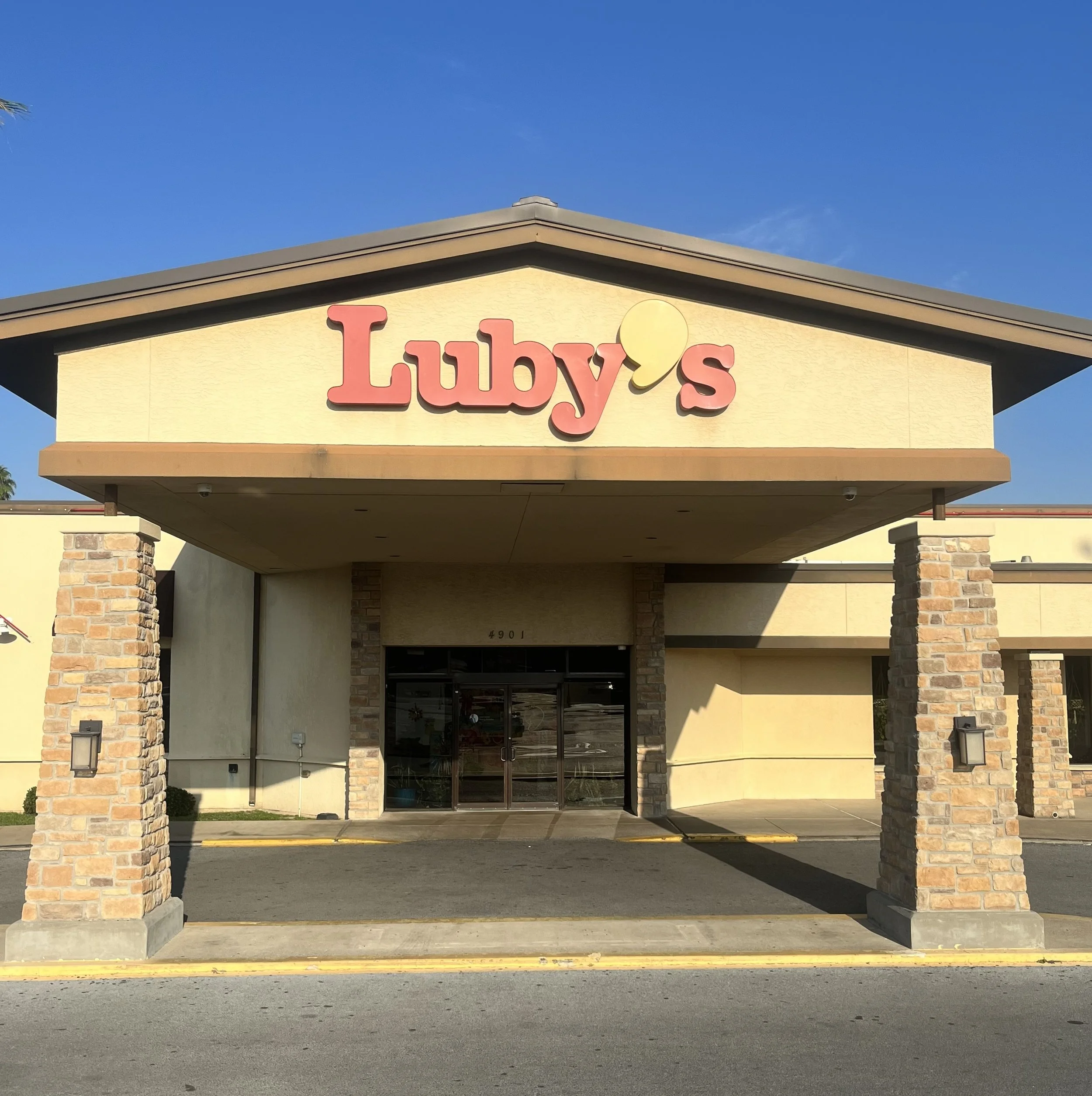 Front view of a building with a sign that says 'Luby's' on top, supported by brick columns, with a clear blue sky above.