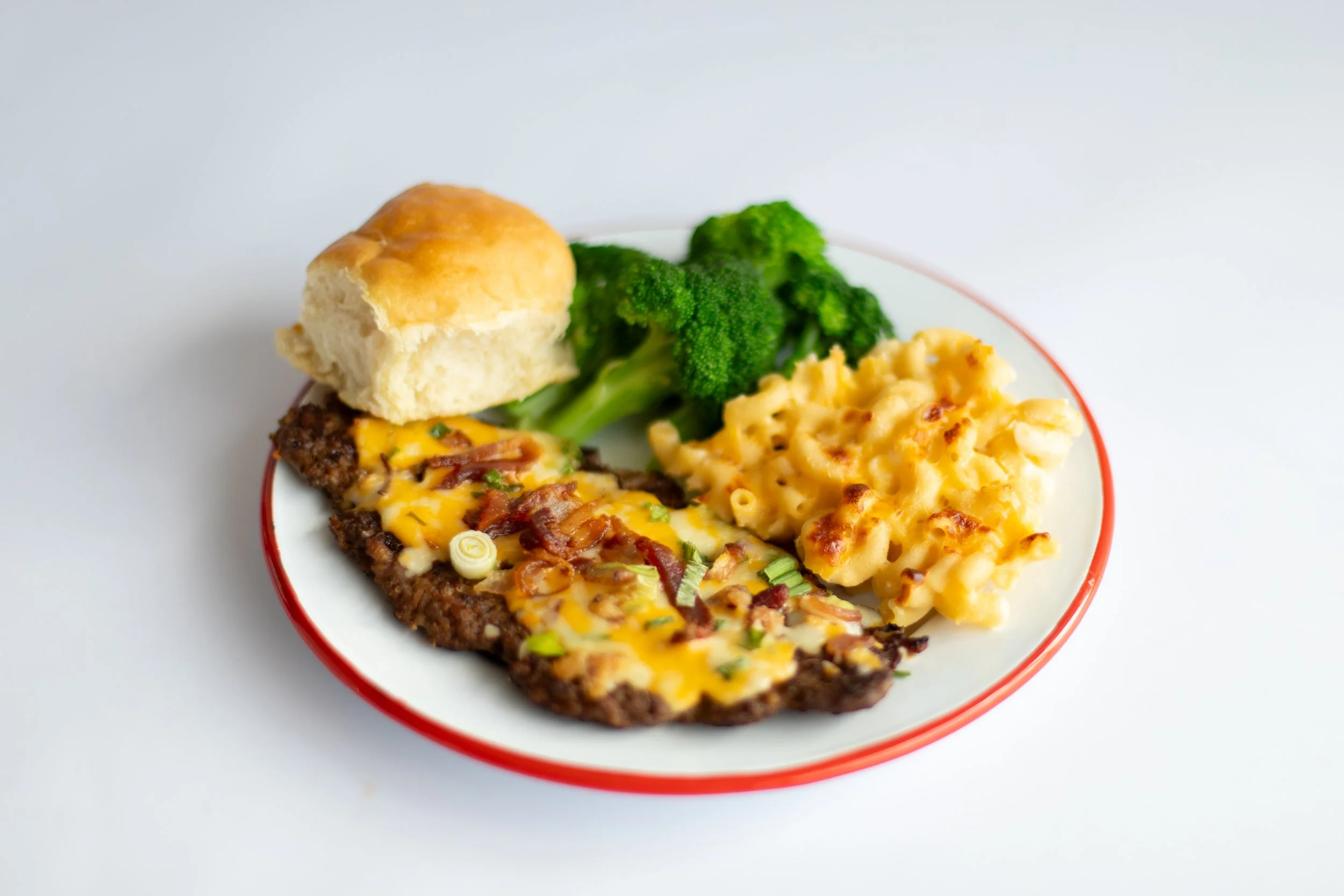 Plate of comfort food including macaroni and cheese, broccoli, a biscuit, and a piece of meatloaf with gravy.