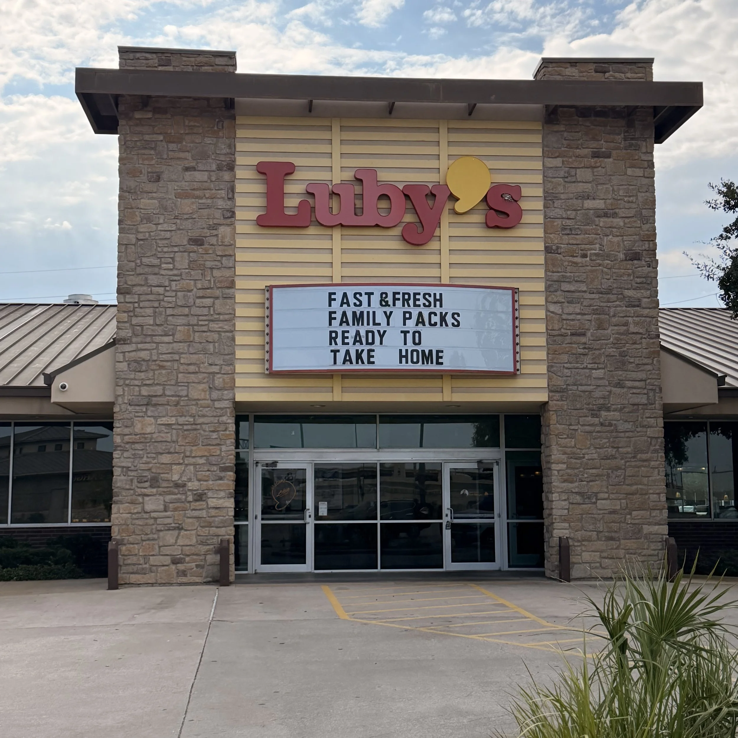 Luby's restaurant exterior with a brick facade and a sign that reads "Luby's" and menu board below indicating fast and fresh family packs available for takeout.