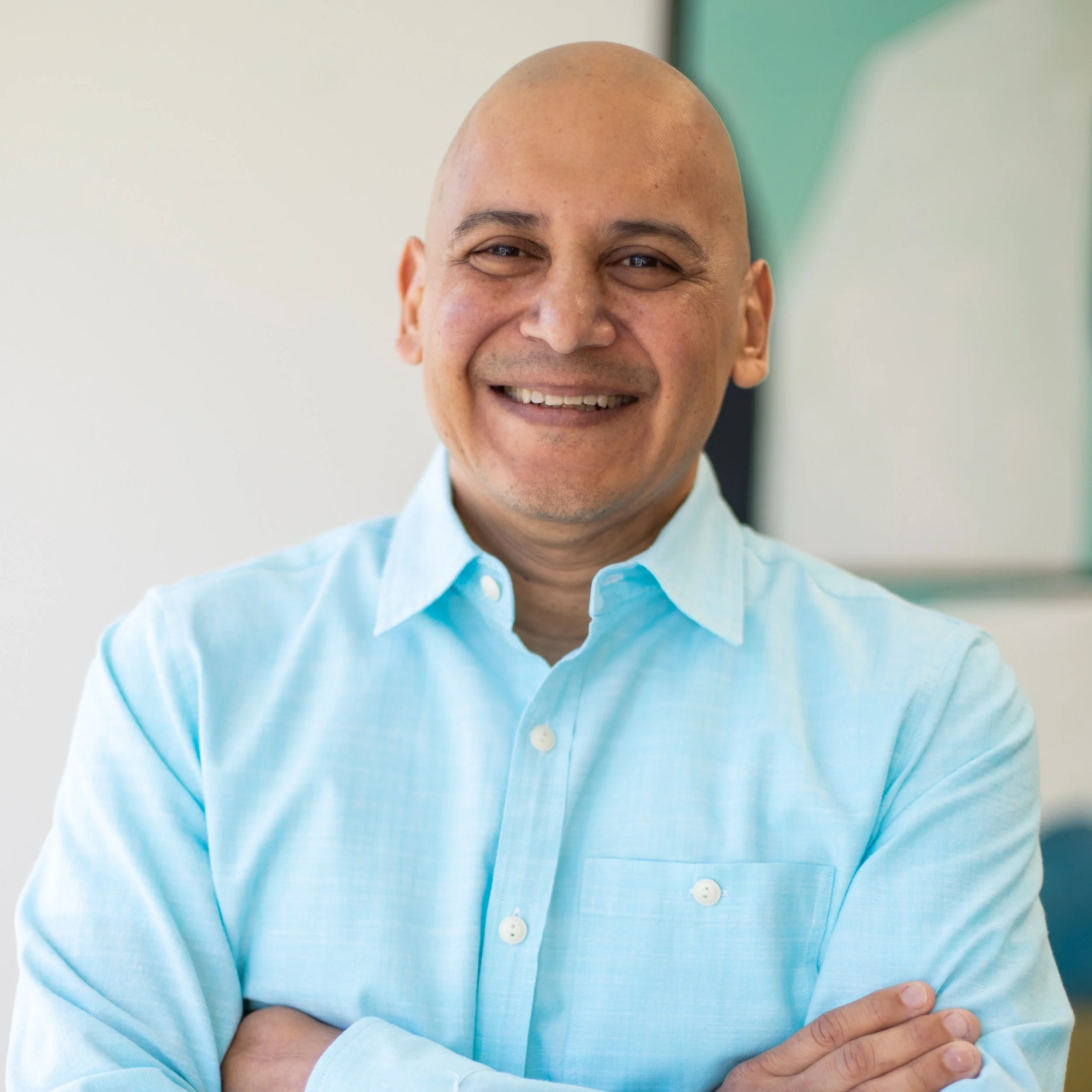 Smiling man with a bald head wearing a light blue shirt, crossing his arms.