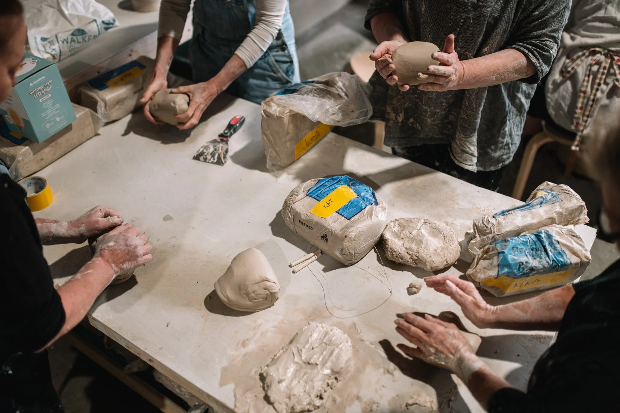Hands shaping and preparing clay at a workbench during a beginner pottery class in Huonville, Tasmania