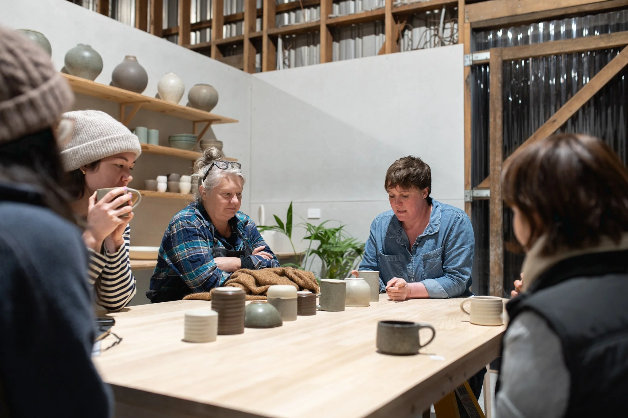 Students gathered around a table discussing handmade ceramics with Lindsey Wherrett during a pottery course in Tasmania
