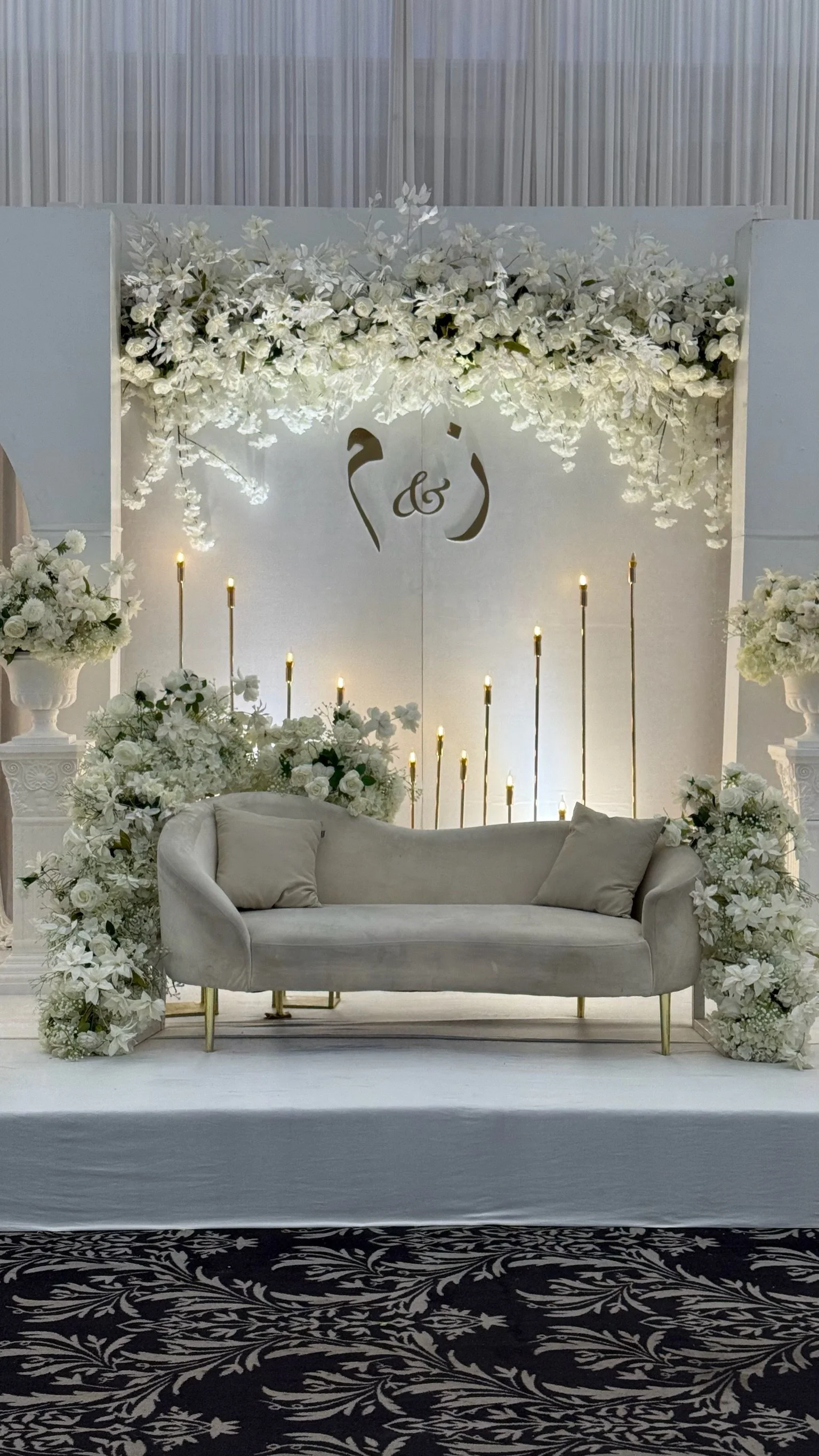 Elegant wedding floral backdrop with white flowers, candles, and a cream-colored sofa.