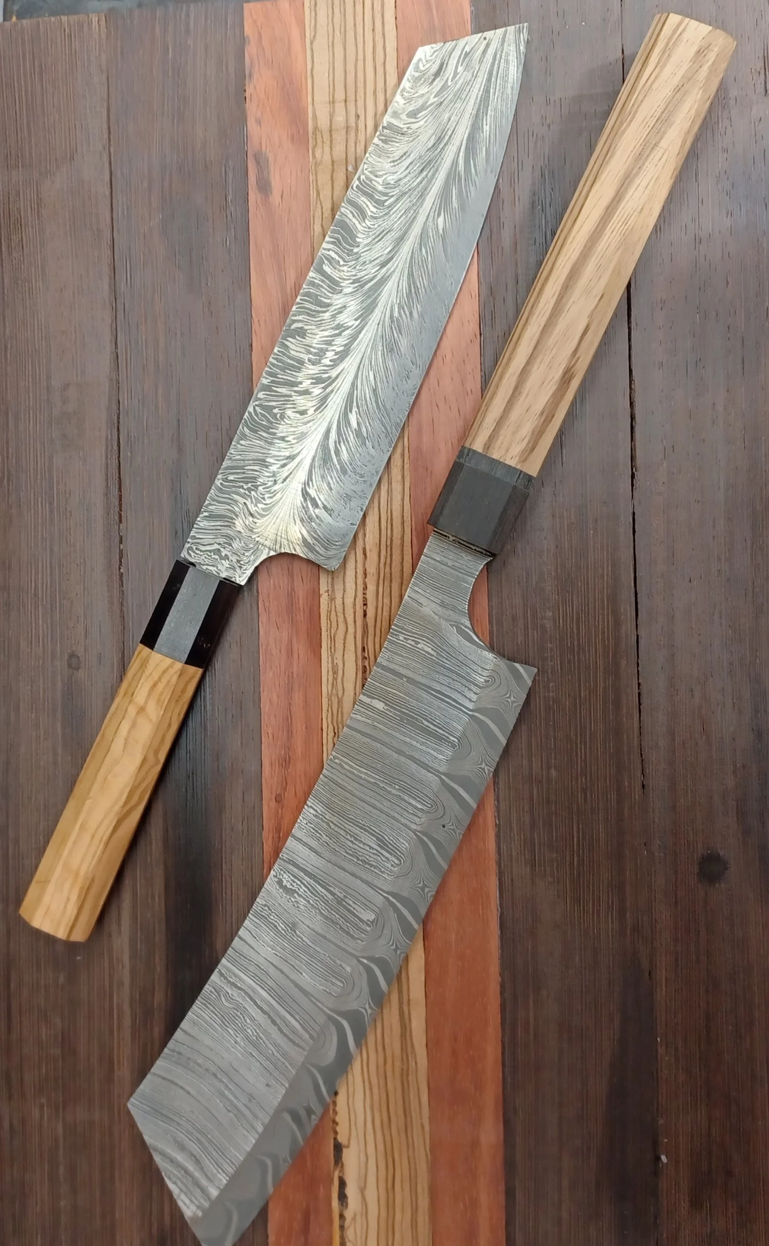 Two Damascus steel knives with wooden handles resting on a multicolored wooden surface.