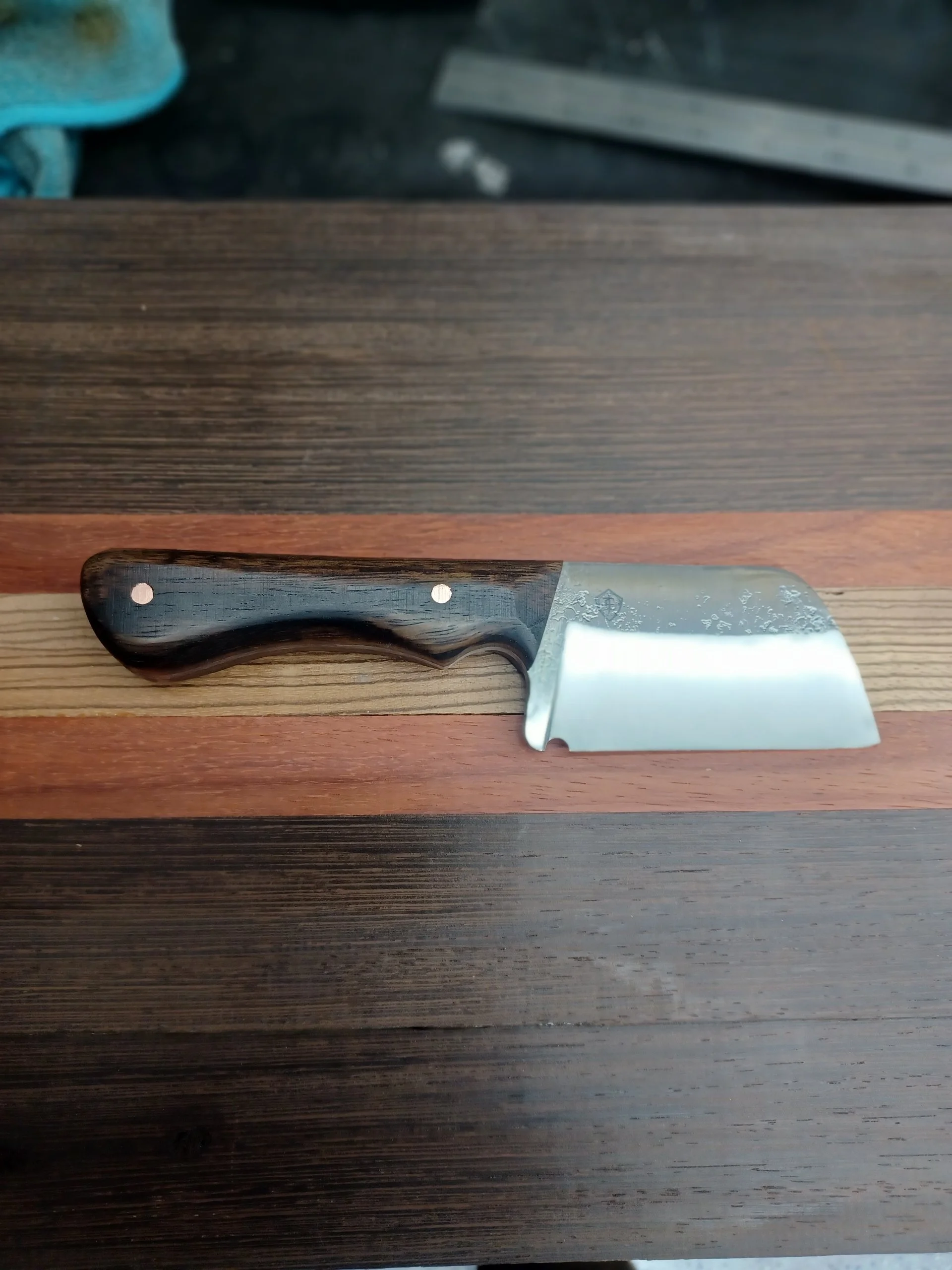 A small kitchen knife with a wooden handle resting on a multi-colored wooden surface.