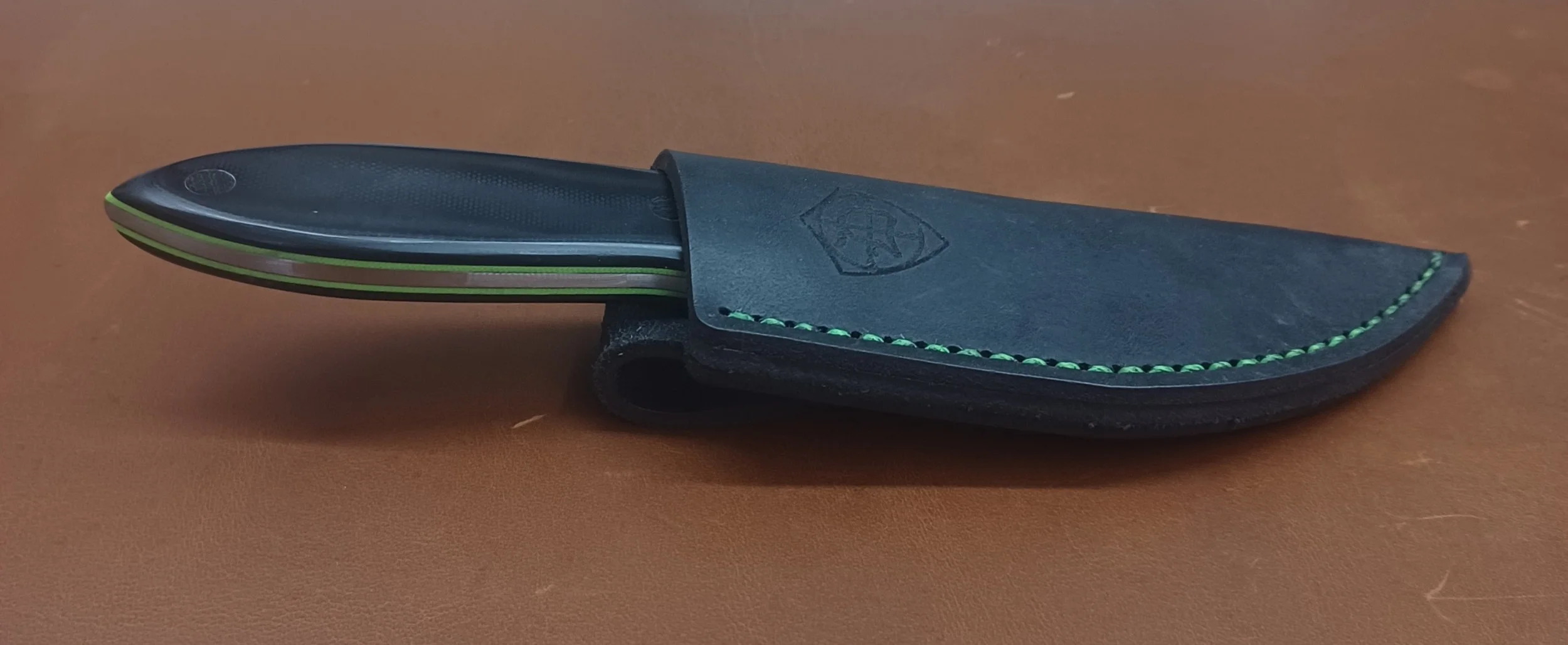 A fixed-blade knife with a black handle and green accents in a black leather sheath.