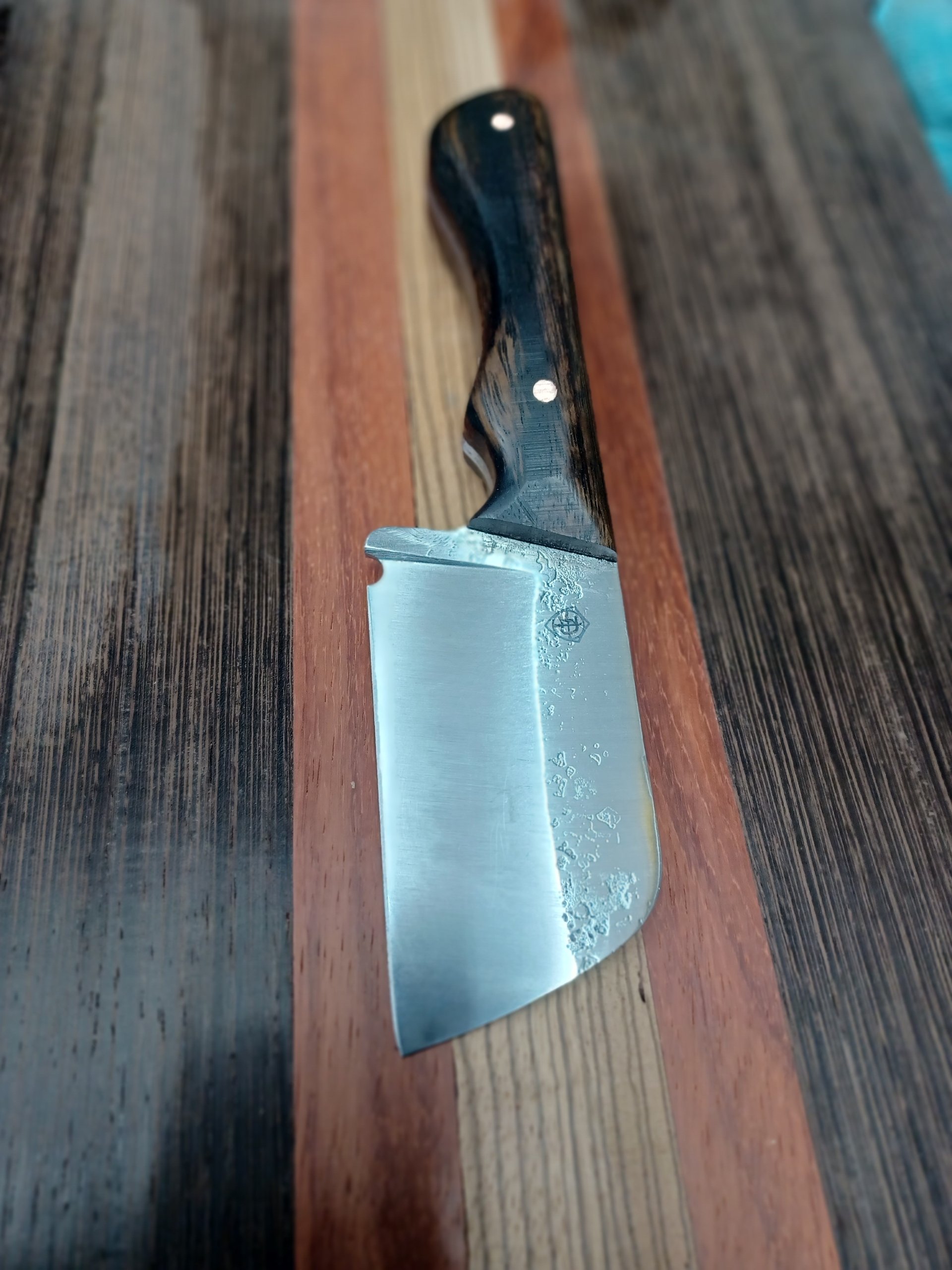 A kitchen knife with a black and wood grain handle resting on a multicolored wooden surface.