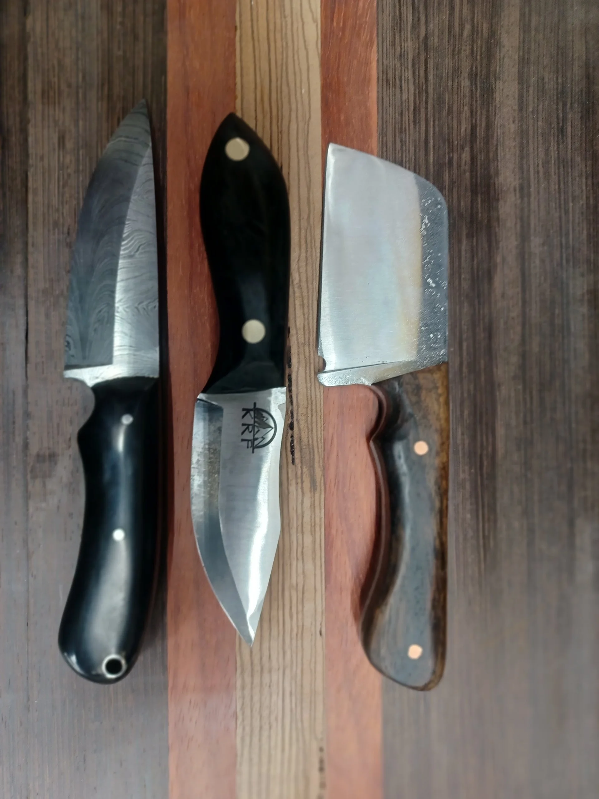 Three knives with different handles and blades are placed on a wooden surface.