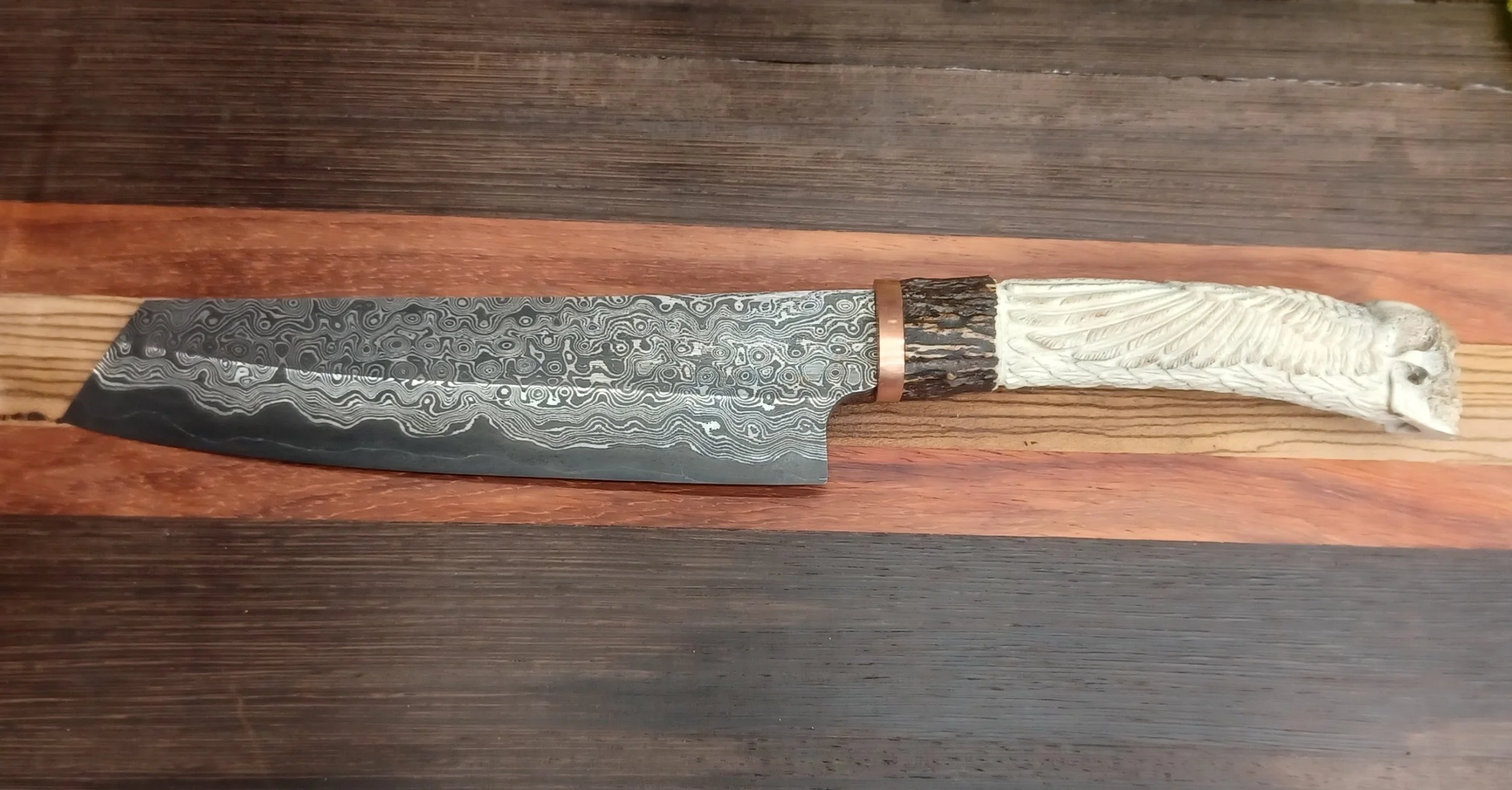 A decorative chef's knife with a Damascus steel blade and a handle made from antler and wood.